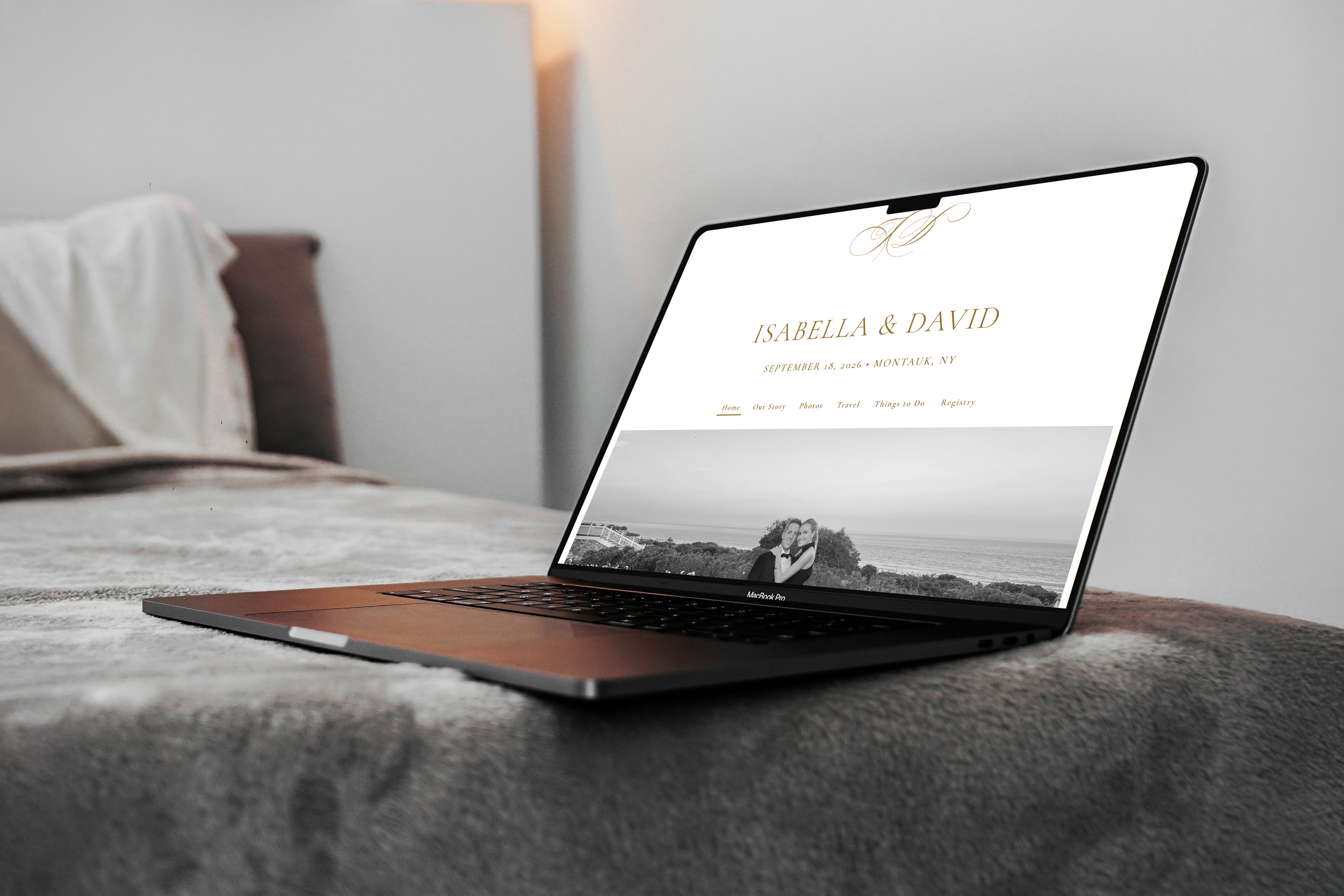 A laptop displaying a wedding website for Isabella and David, with their names, wedding date, and location, and a black-and-white photo of a couple embracing with ocean in the background.