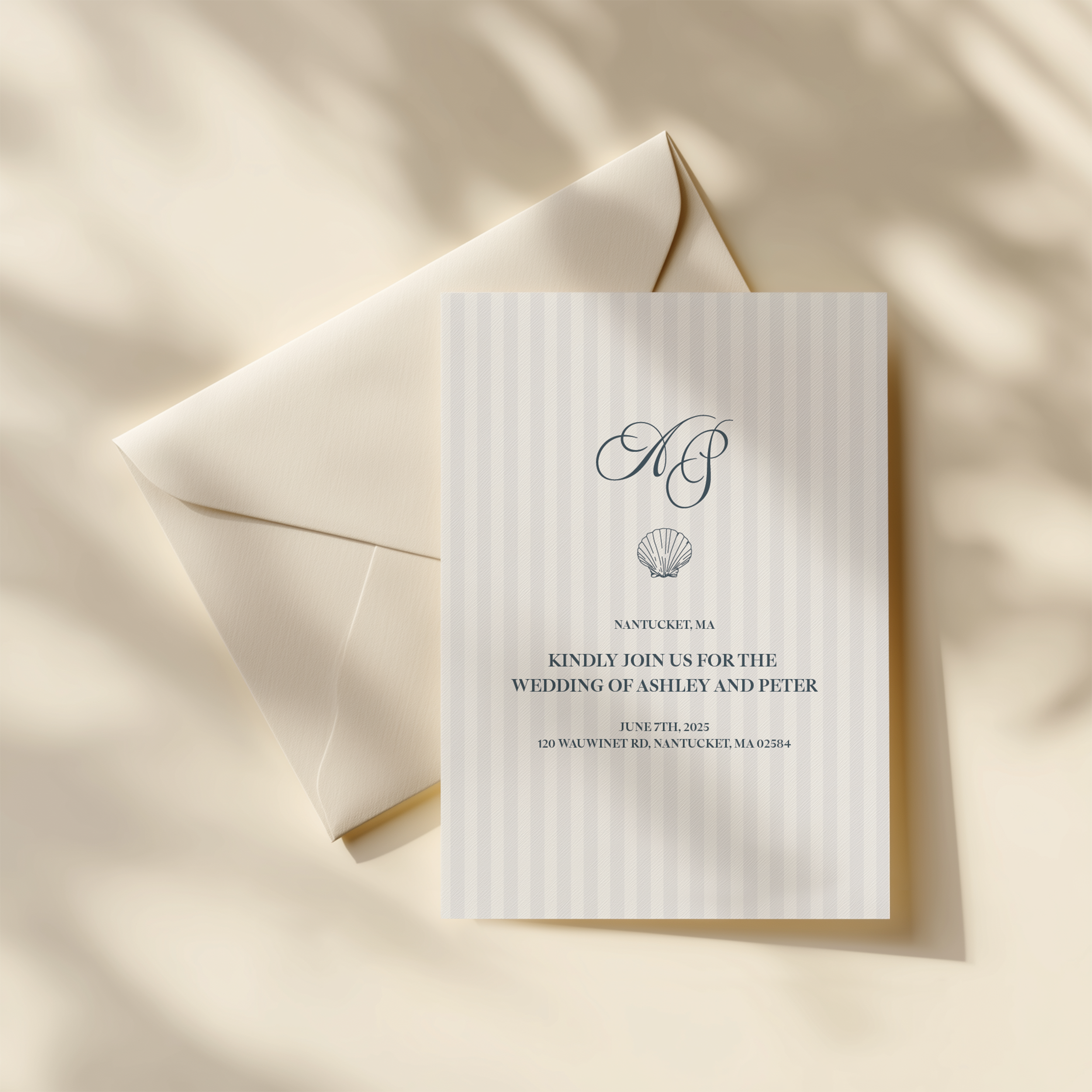 Wedding invitation card with a scallop shell graphic, featuring initials, date, and location, placed on an off-white envelope on a cream-colored surface.