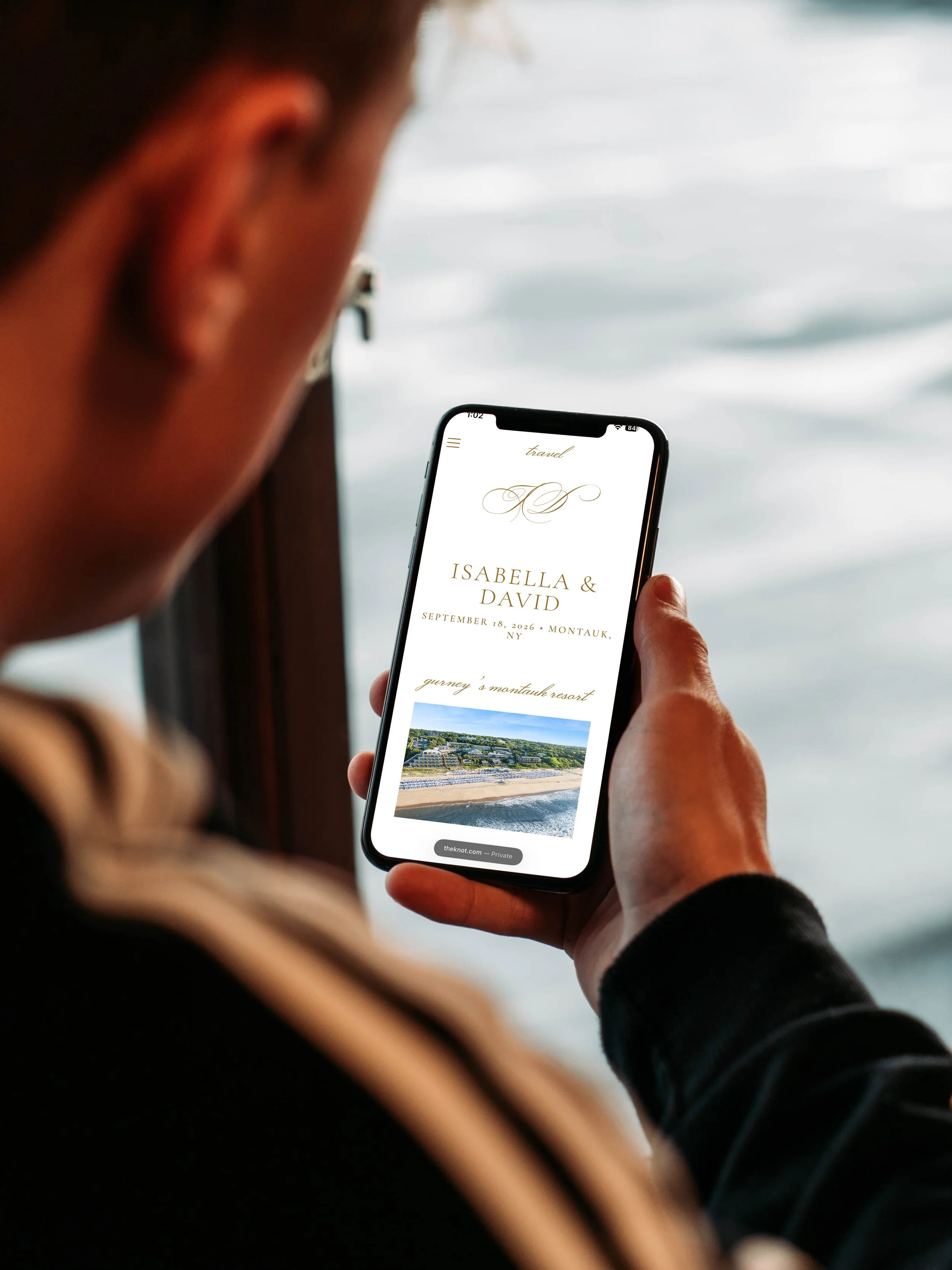 Person holding a smartphone displaying a wedding invitation for Isabella and David, with details about the date, location, and a scenic beach photo.