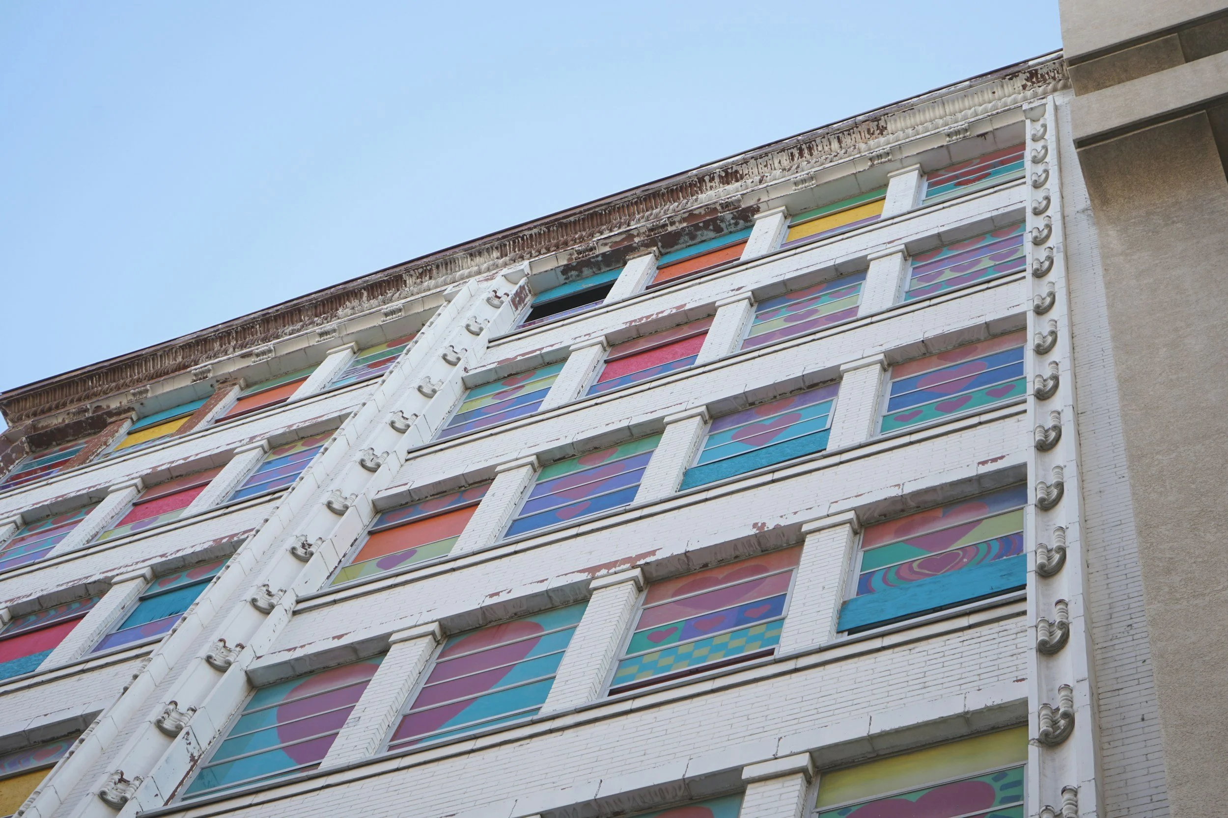 Close-up of a multi-story building with colorful stained glass windows and peeling white paint, viewed from below against a clear blue sky.