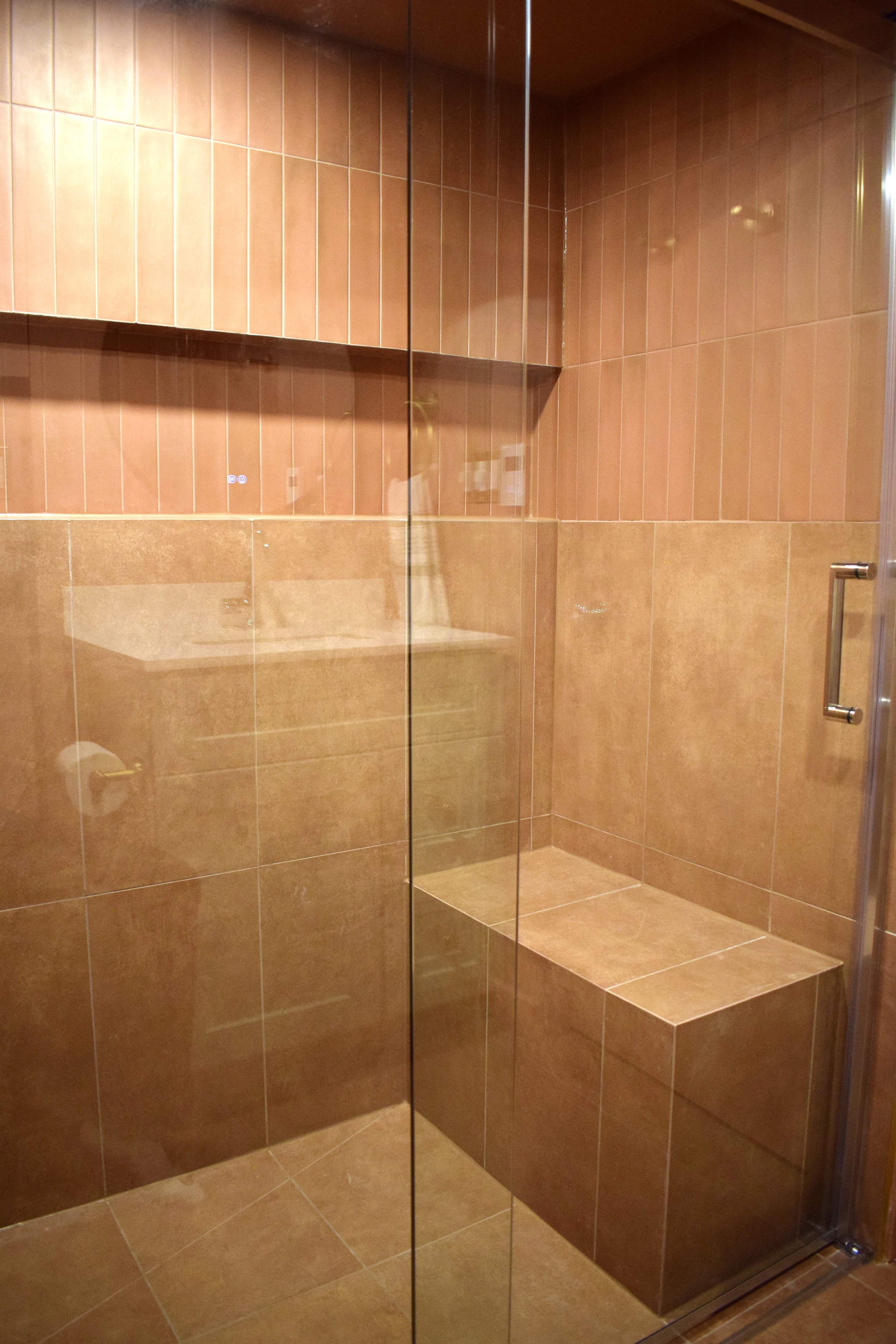 A tiled shower with brown tiles, a built-in bench, and a glass door.