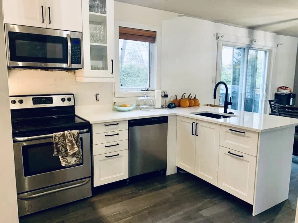 Kitchen with white cabinets, stainless steel appliances, a black sink, and a window above the counter with pumpkins}