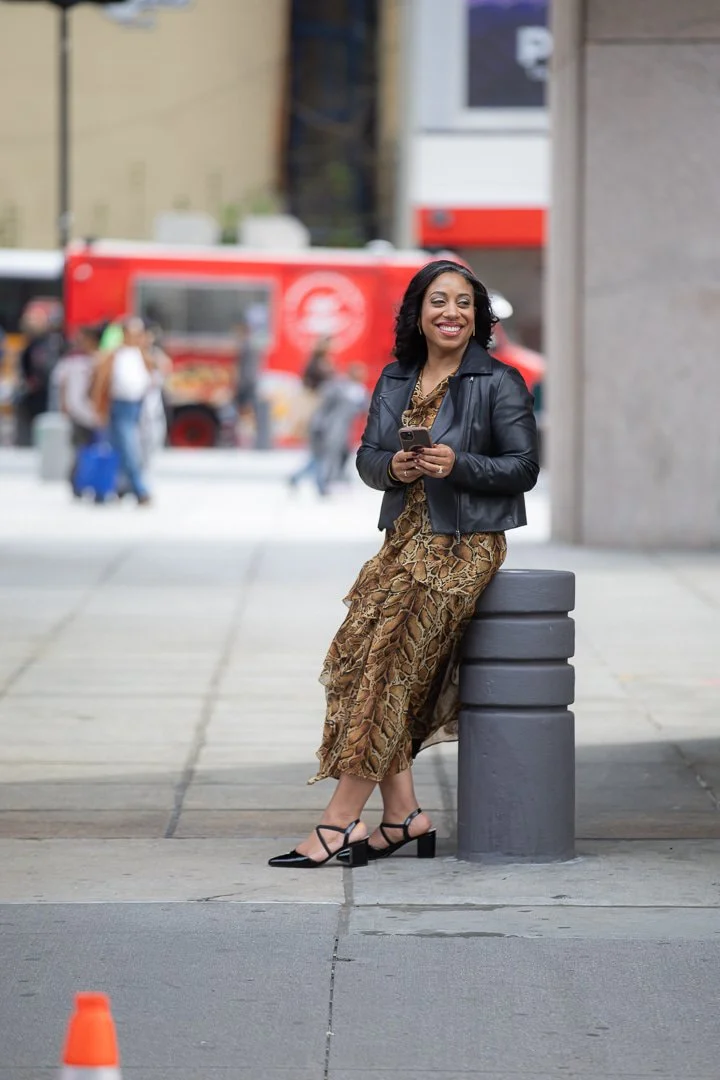 Ariane Lovell Director of PR - in leopard dress, black jacket and heels, smiling and holdin phone