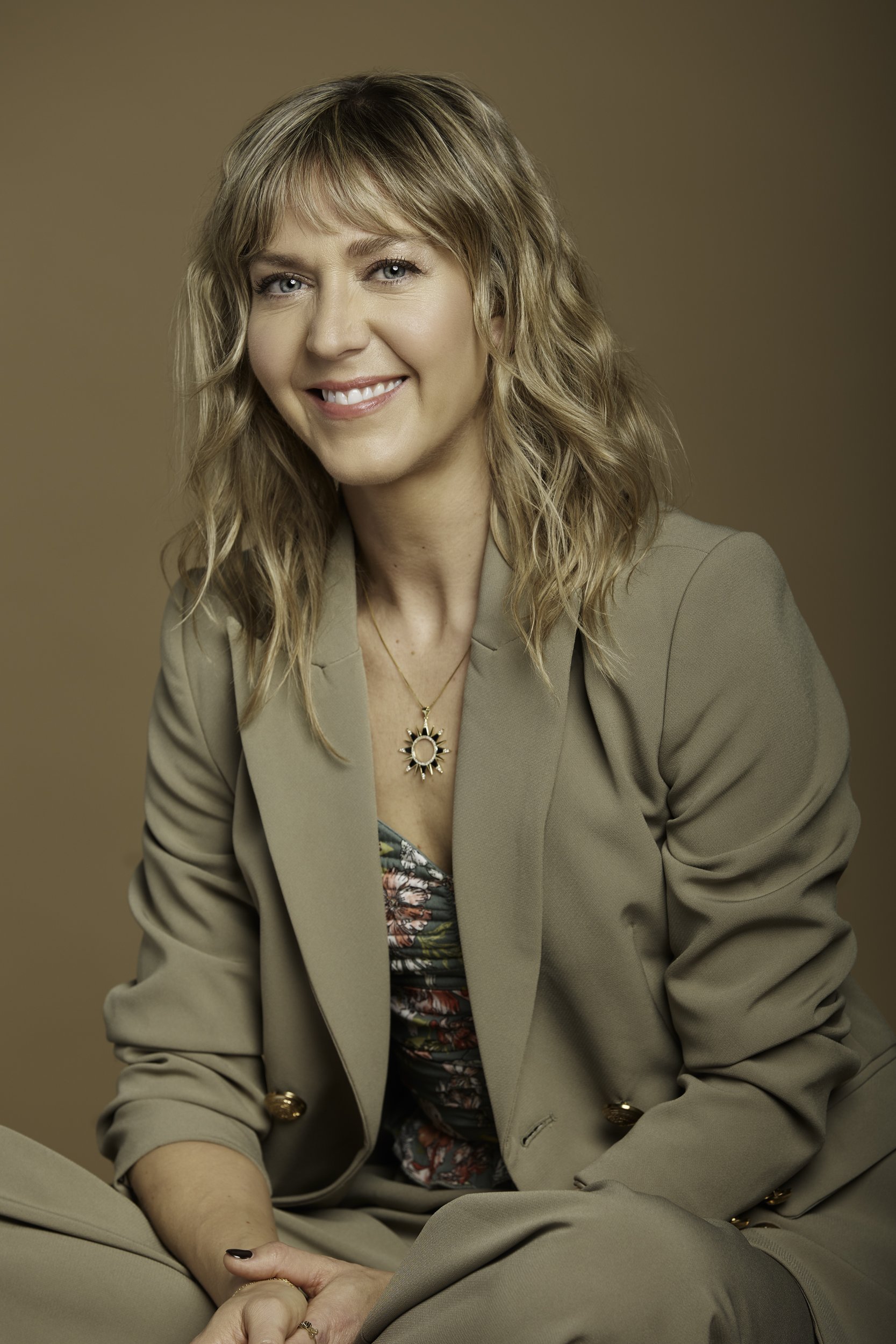 Portrait de Julie Gagnon, relationniste de presse, une femme souriante avec des cheveux blonds bouclés, portant un tailleur beige.