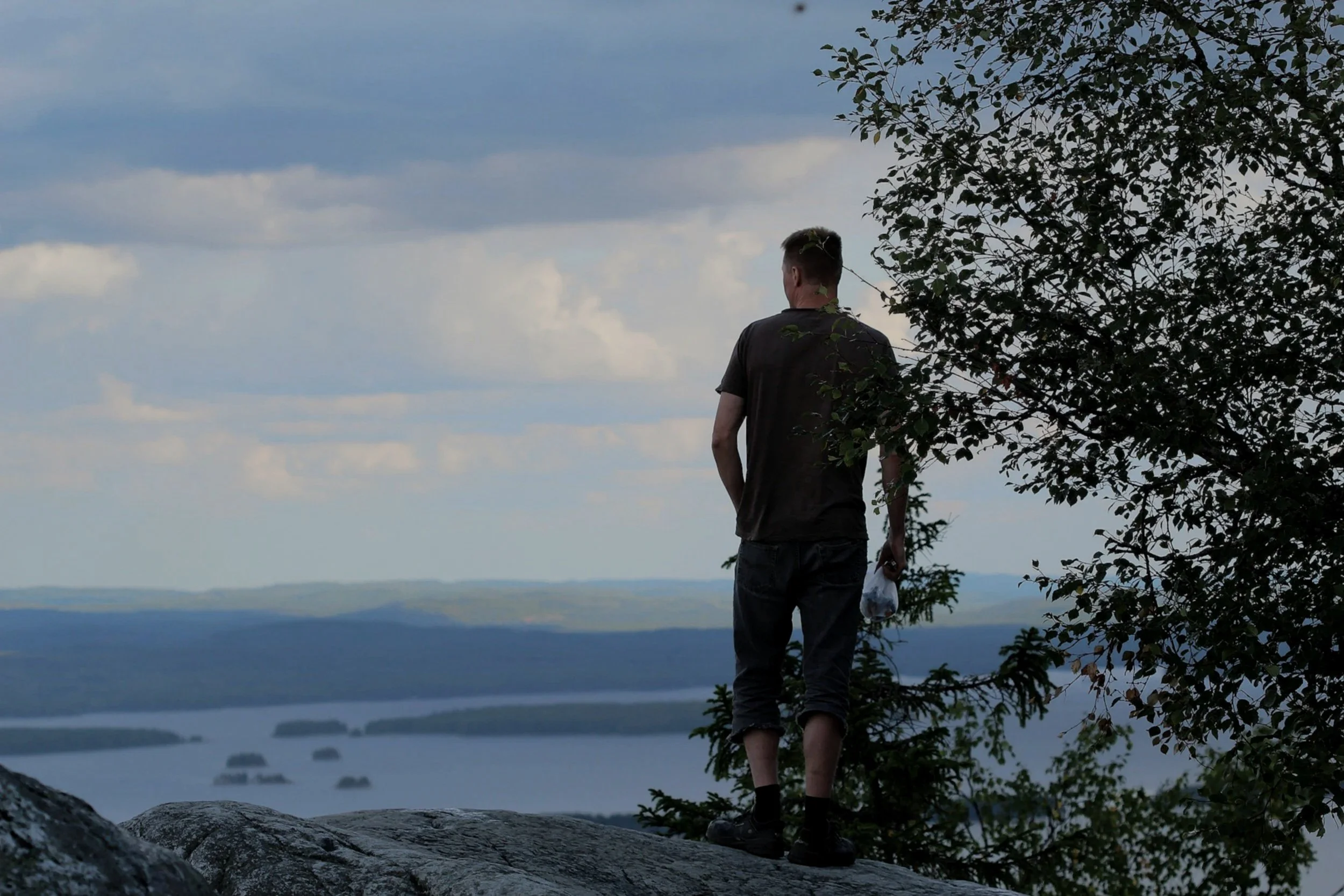 man standing on a mountain overlooking a lake and horizon