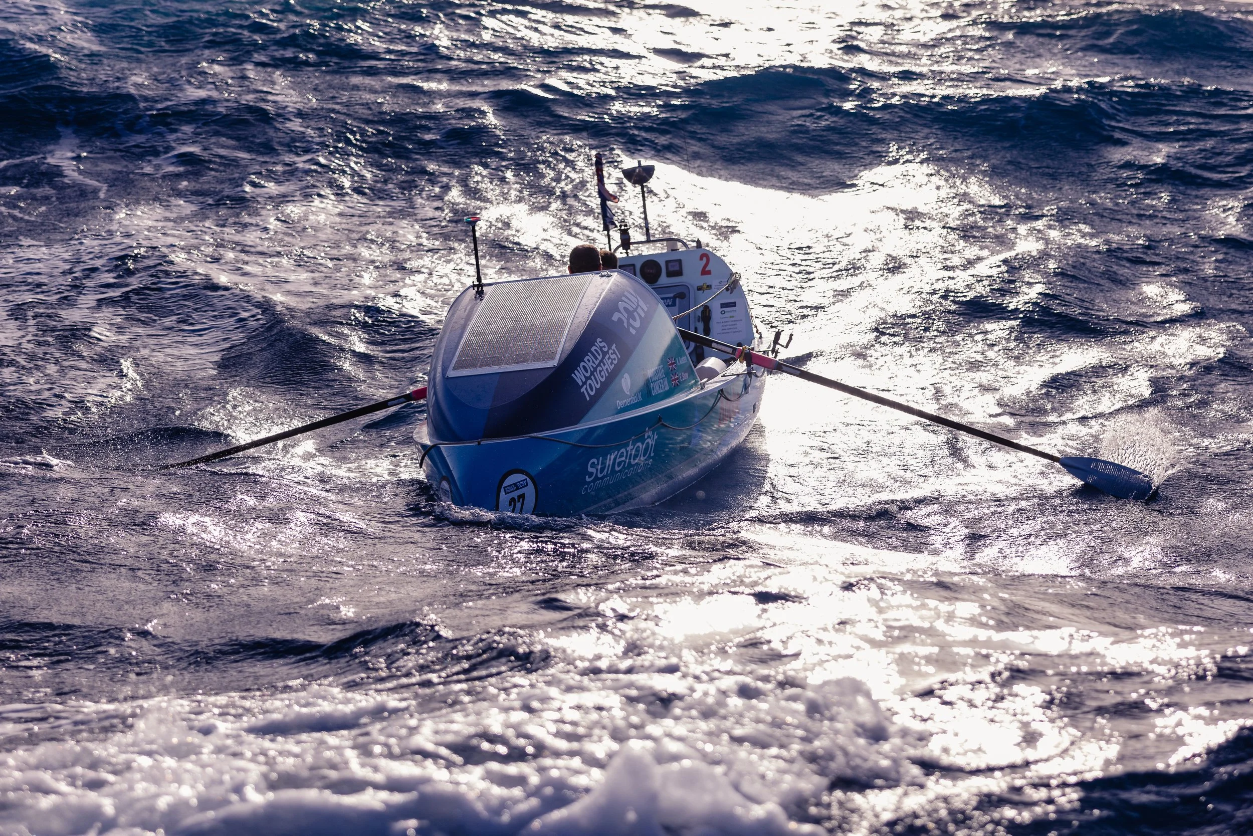A blue racing boat on the water with a person onboard, surrounded by waves and sunlight reflections.
