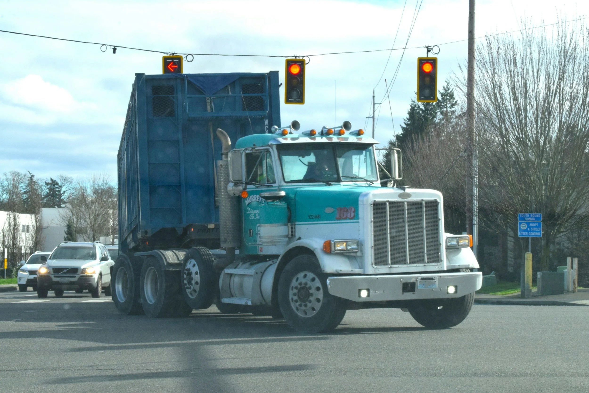 Semi-truck with container making a tight left turn near a traffic light.
