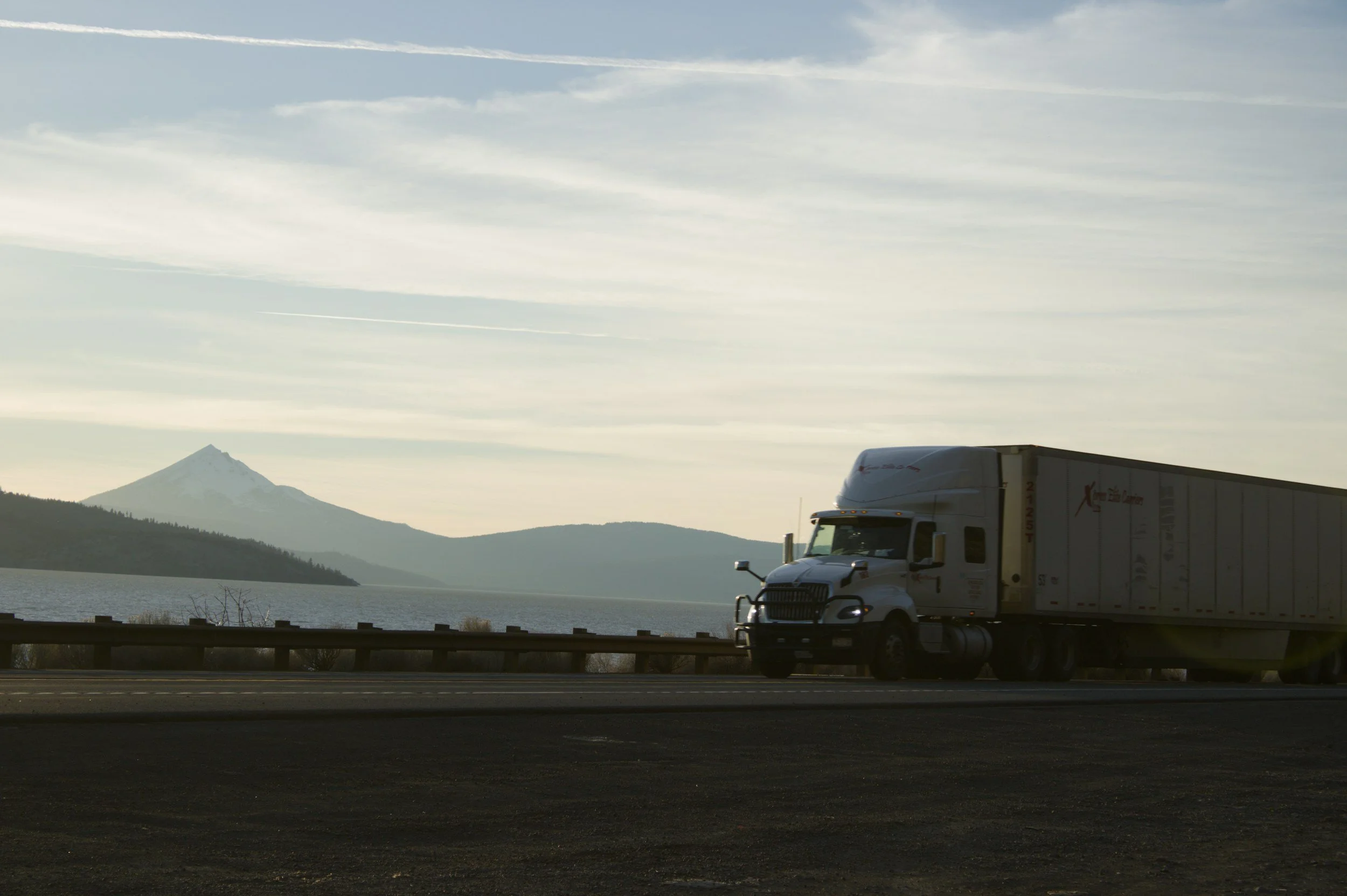 Semi-truck driving on a highway at night surrounded by mountainous terrain.