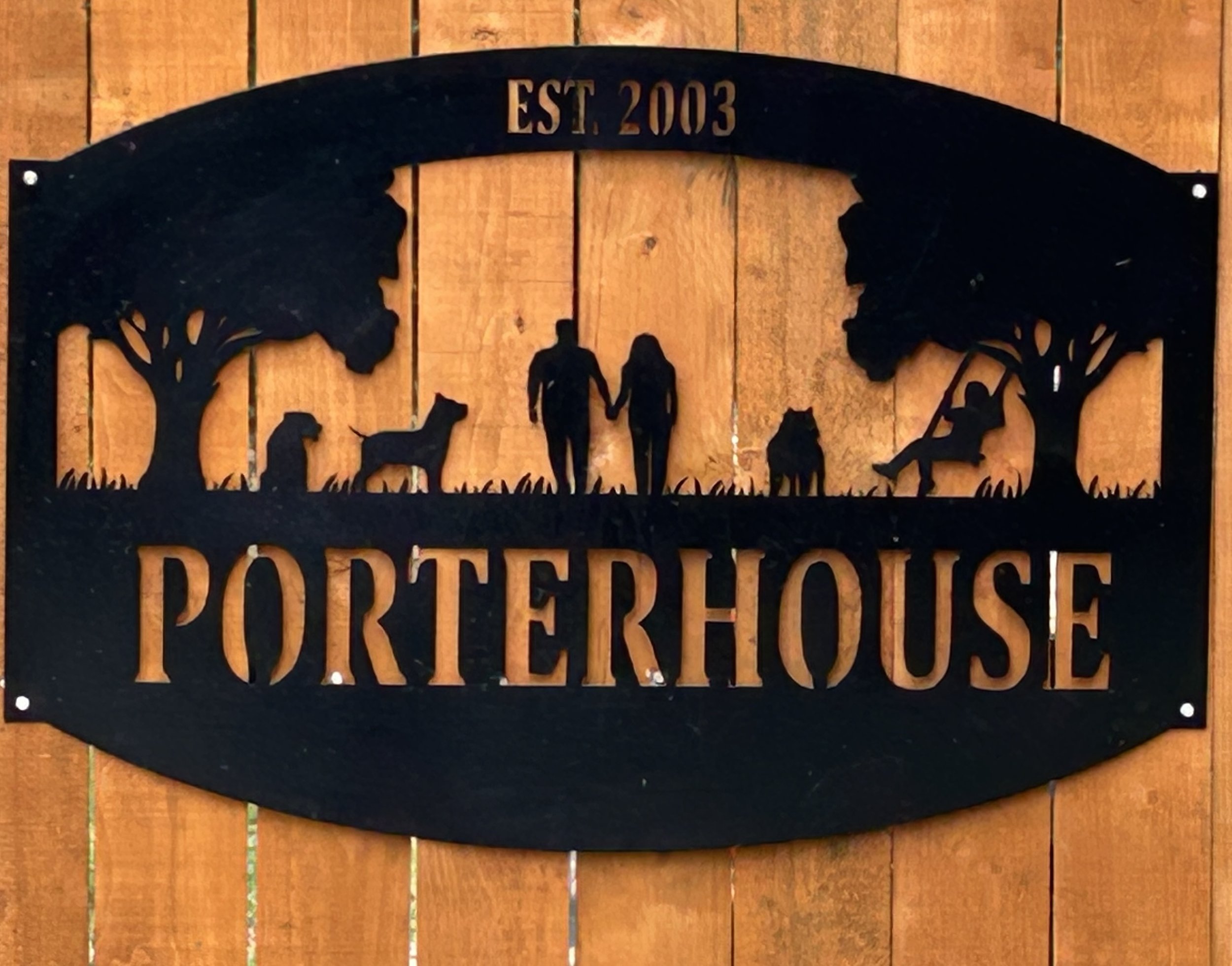 Metal sign with silhouette trees, people, dogs, and a child on a swing, featuring the words 'Porterhouse' and 'EST. 2003'.