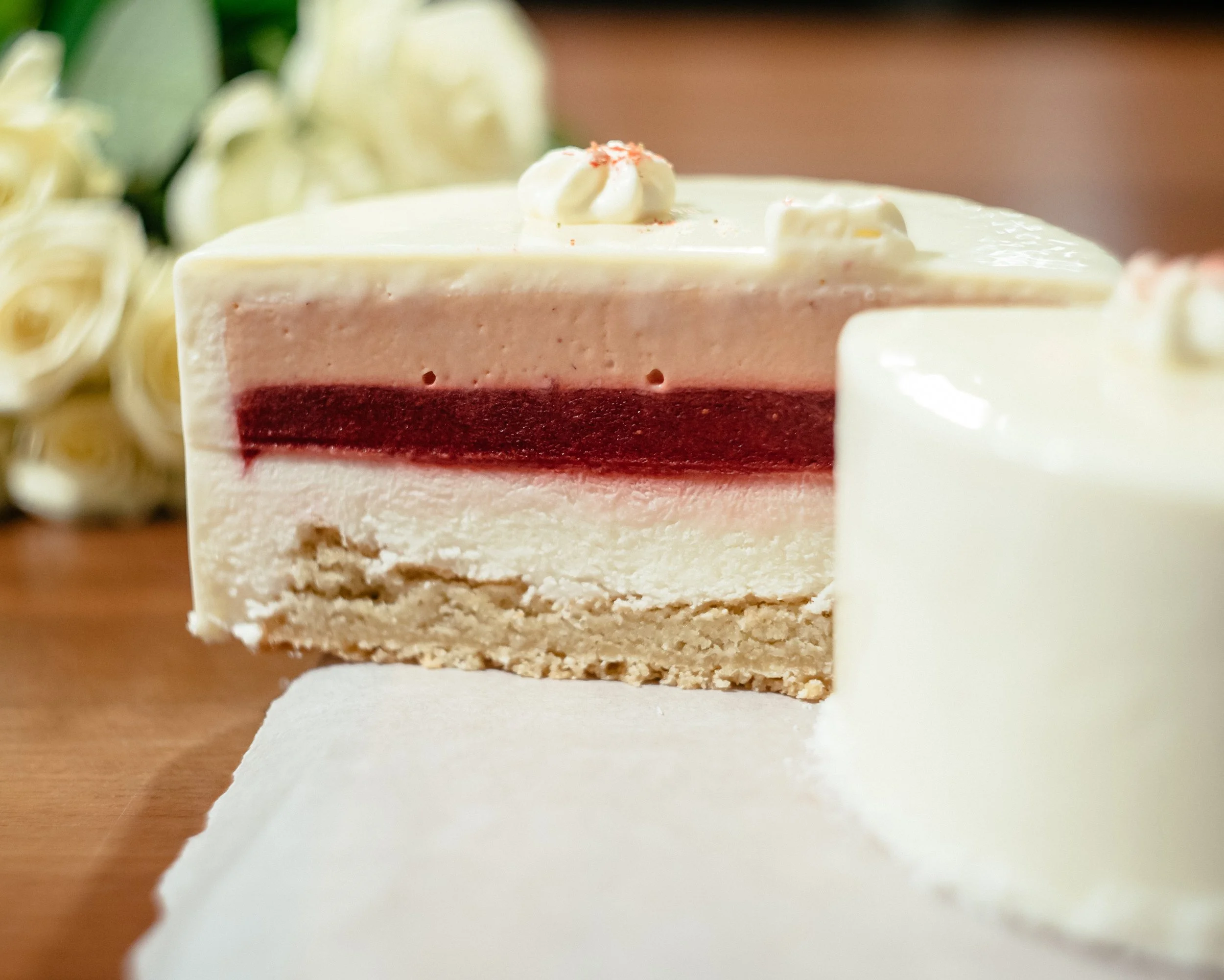 Close-up of a layered cake with white frosting, a red layer in the middle, topped with whipped cream and red sprinkles, on a white cake stand.