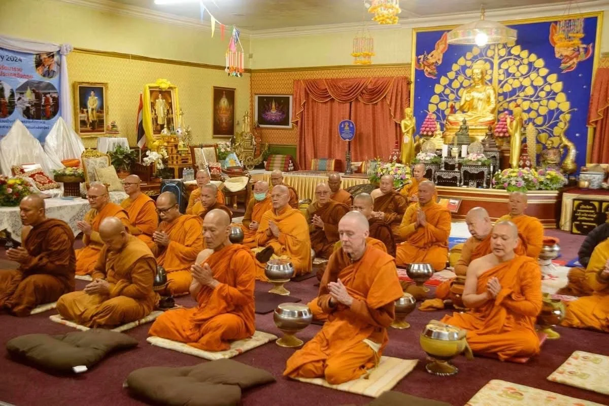 Buddhist monks in orange robes praying in a decorated temple with a statue of Buddha and Buddhist artwork.