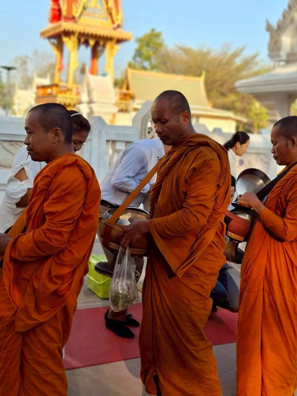 Buddhist monks and laypeople participating in a religious ceremony outdoors, with a temple or shrine in the background.
