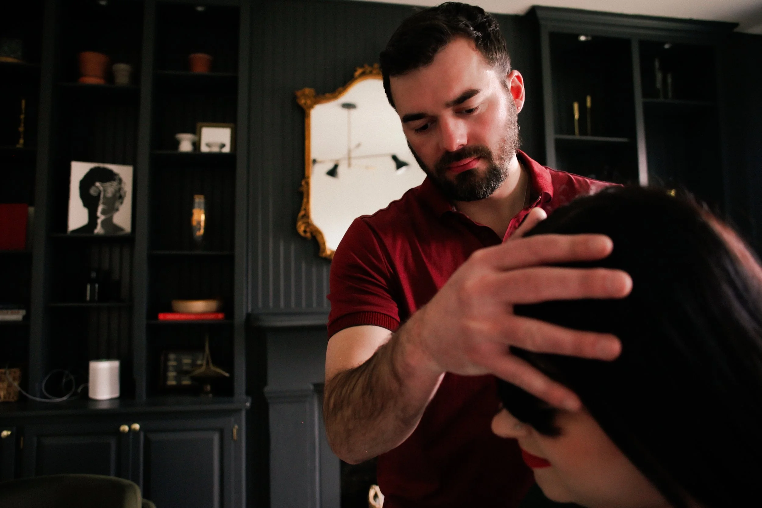 Dr. Evan performing chiropractic care, holding a woman's head gently in a room with dark walls and shelves, a mirror with a gold frame, and a chandelier reflected in the mirror.