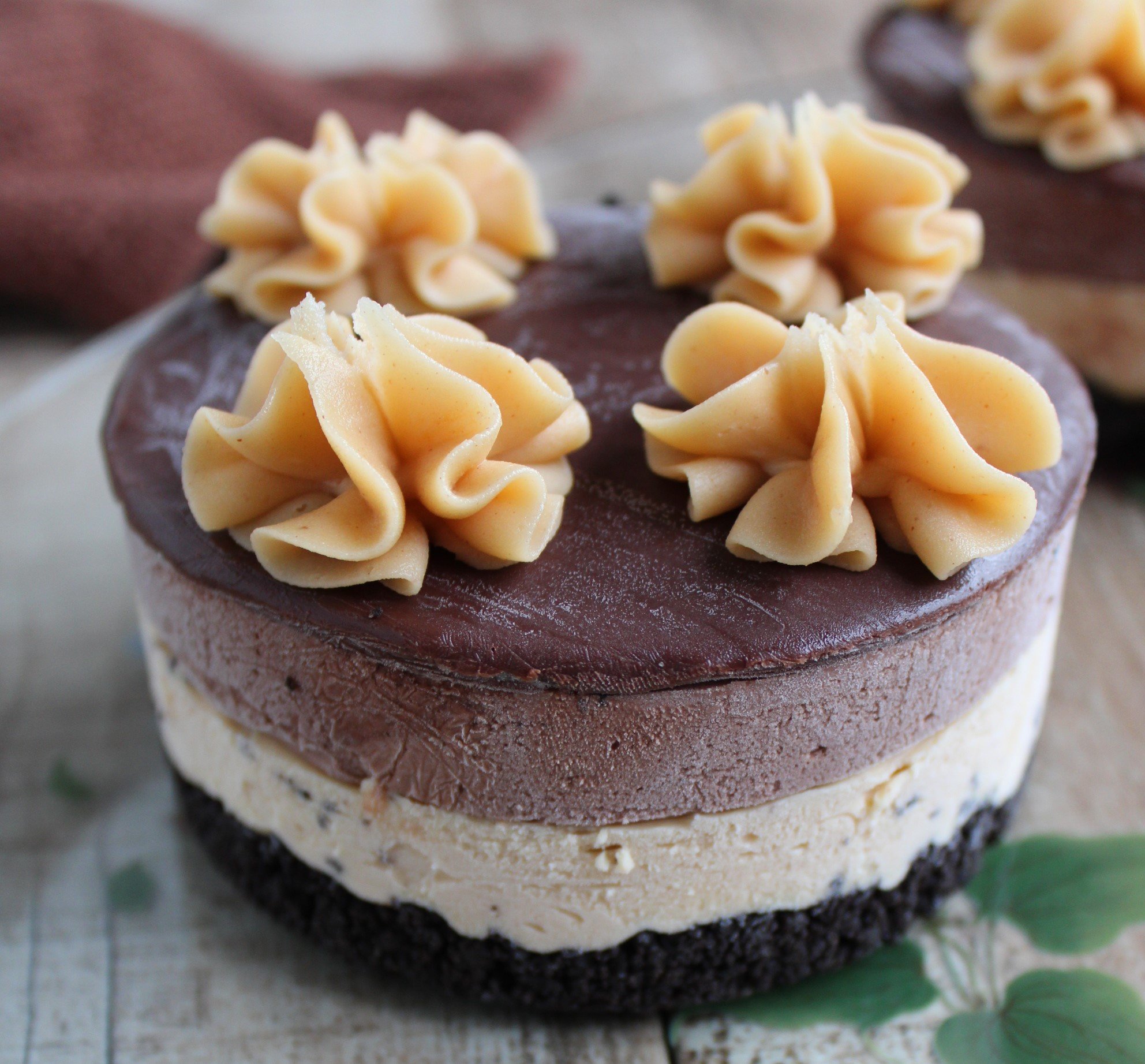 Close-up of a cupcake with multiple layers. The bottom layer is a cream-colored cake, topped with a dark chocolate layer, and garnished with yellow piped frosting decorations.
