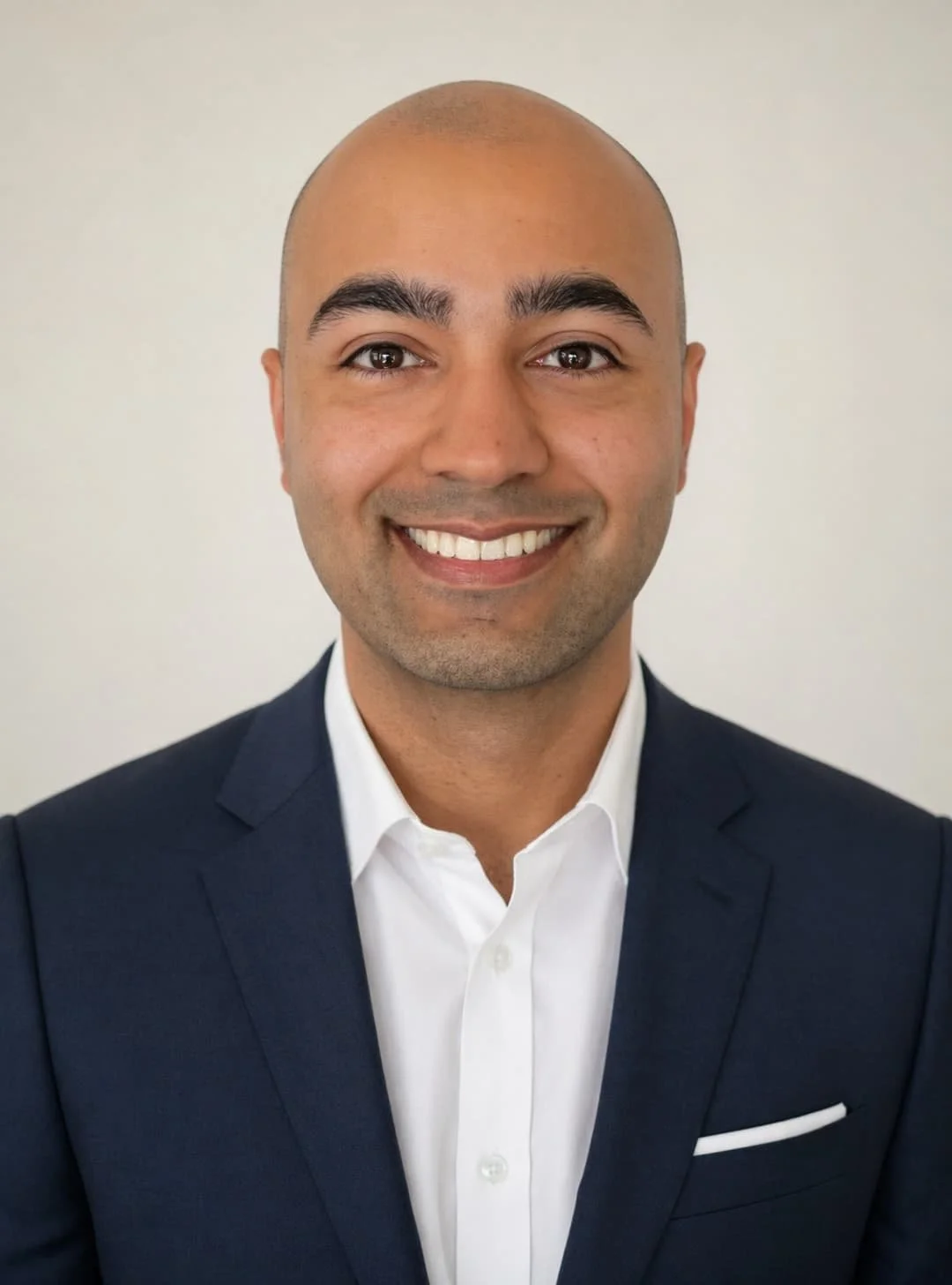 Headshot of a smiling man in a dark suit and white shirt against a plain background.