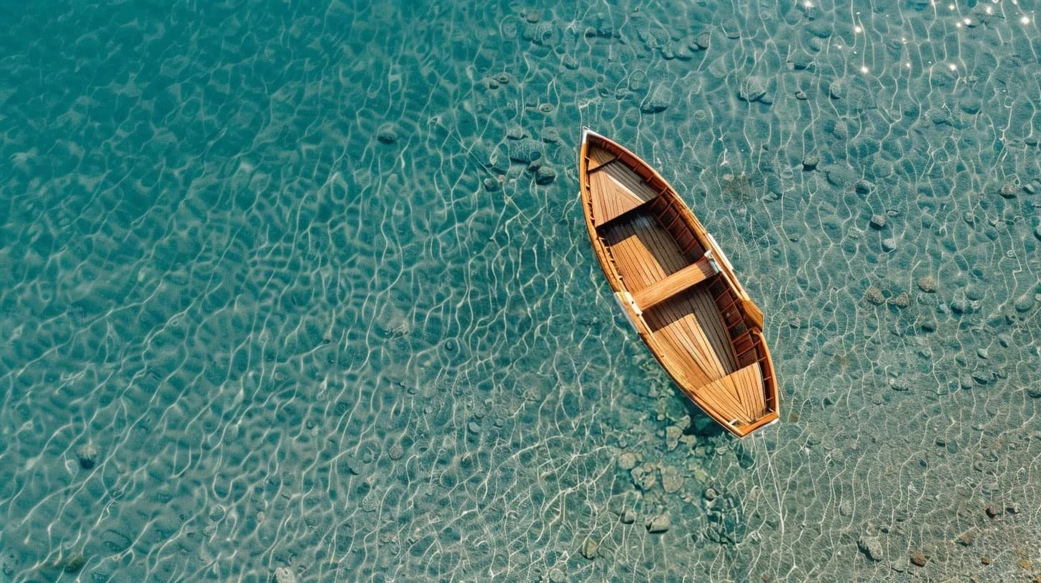 A wooden rowboat floats in clear shallow water with a pebbled bottom visible underneath.