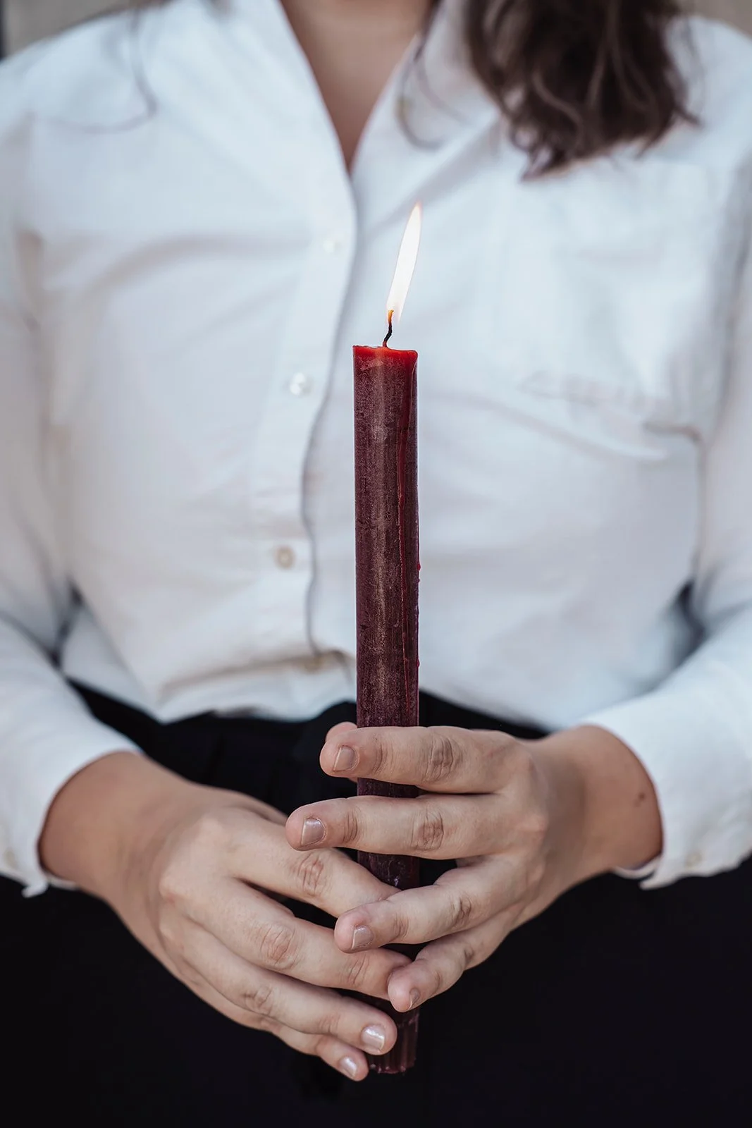 Une personne en chemise blanche tient une grande bougie rouge avec une flamme allumée.