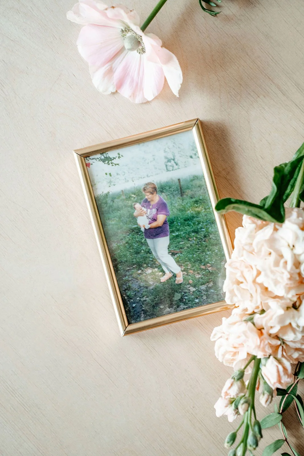 Une photo d'une femme (ma grand-mère) tenant un bébé (moi) en plein air, entourée de fleurs, dans un cadre doré.