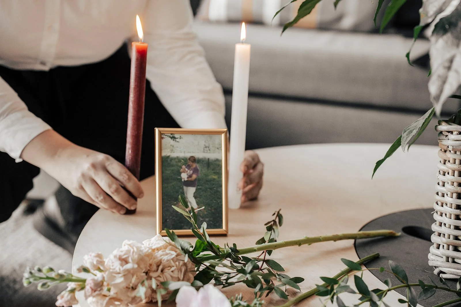 Cérémonie commémorative avec deux bougies allumées, une photo encadrée, des fleurs et des feuilles sur la table.