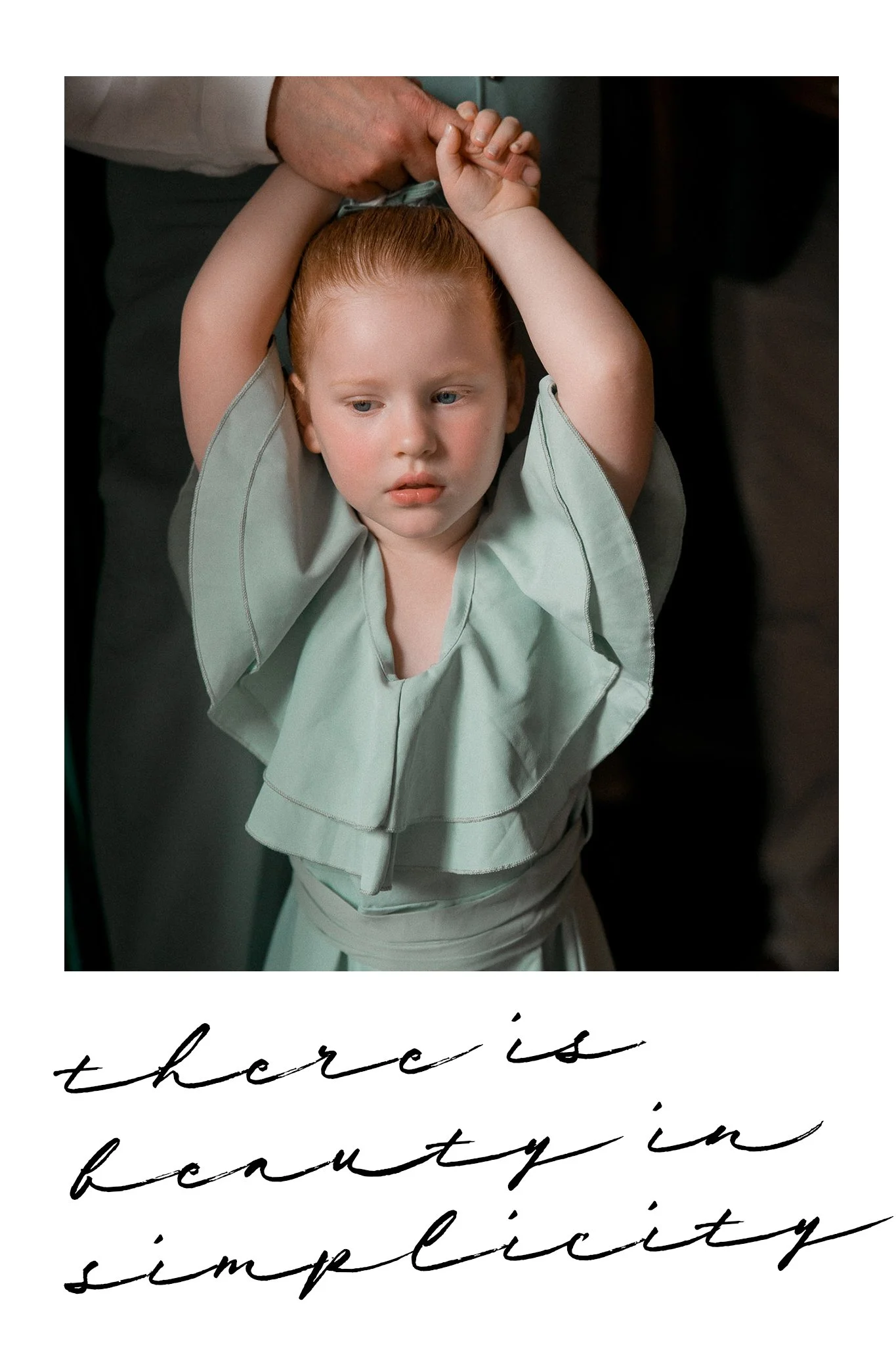 Een jonge rodehaarige meid wordt geholpen door een volwassene terwijl haar armen omhoog worden gedaan, met een tekst onderaan die zegt 'there is beauty in simplicity'.