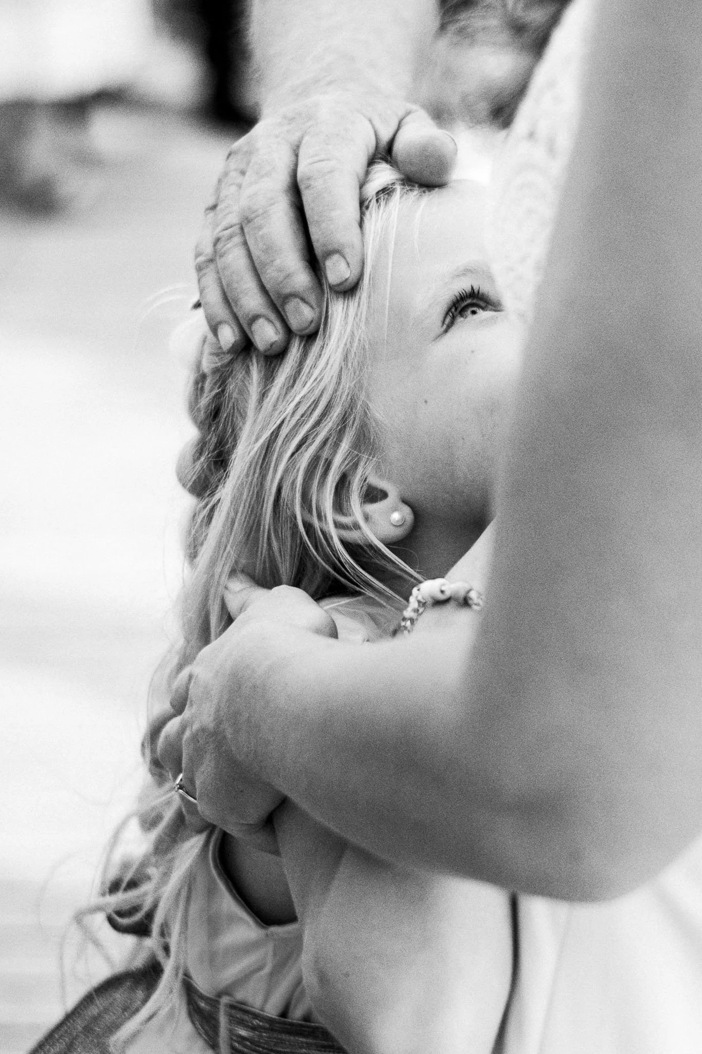 Een close-up zwart-wit foto van een meisje dat door een volwassene wordt geknuffeld, vooral haar gezicht en haar haar zijn zichtbaar.