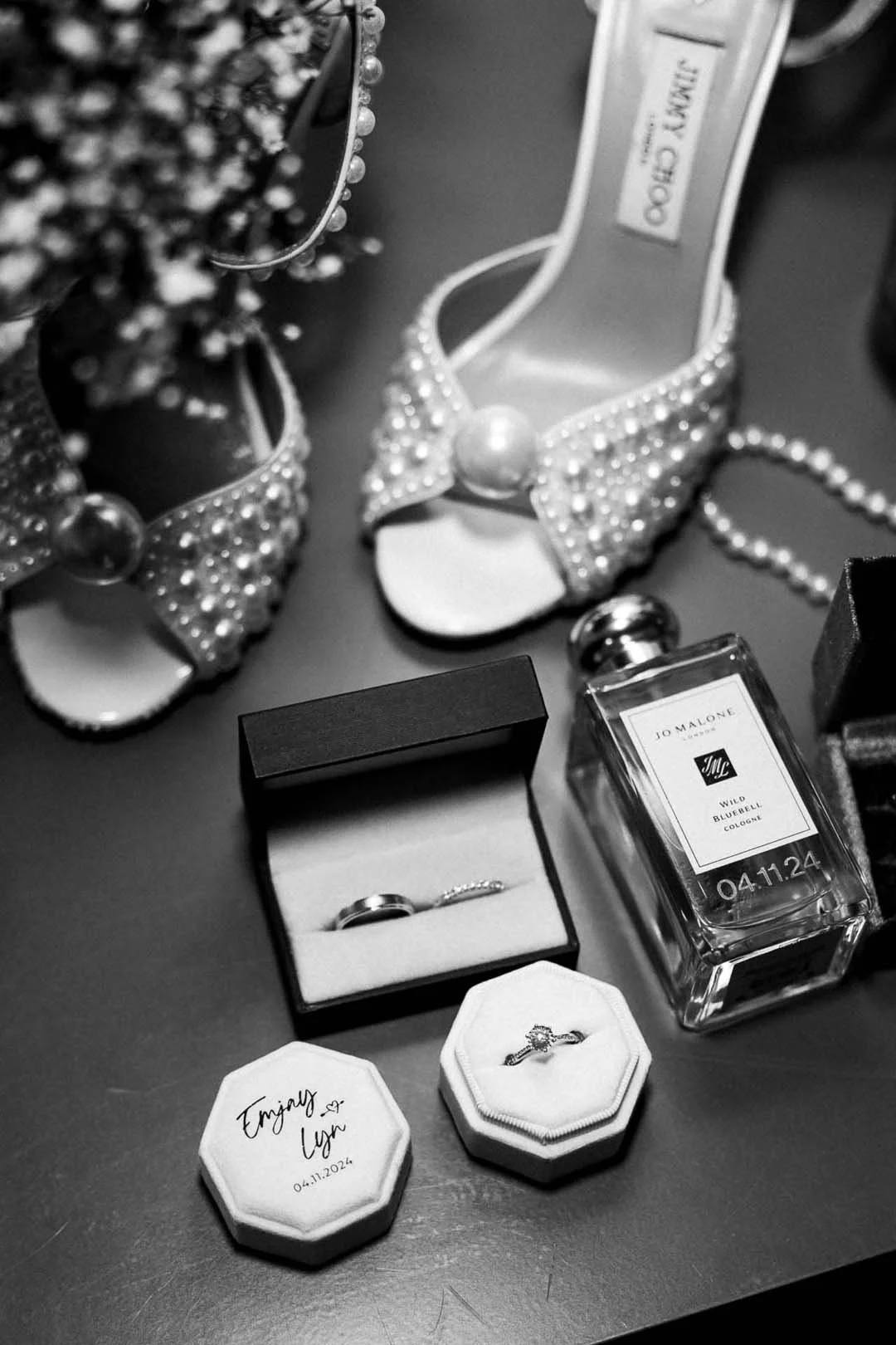 Sieraden, parfum, en huwelijksringen op een tafel, inclusief een paar schoenen met parelversiering en een geborduurde trouwkaart met datum
