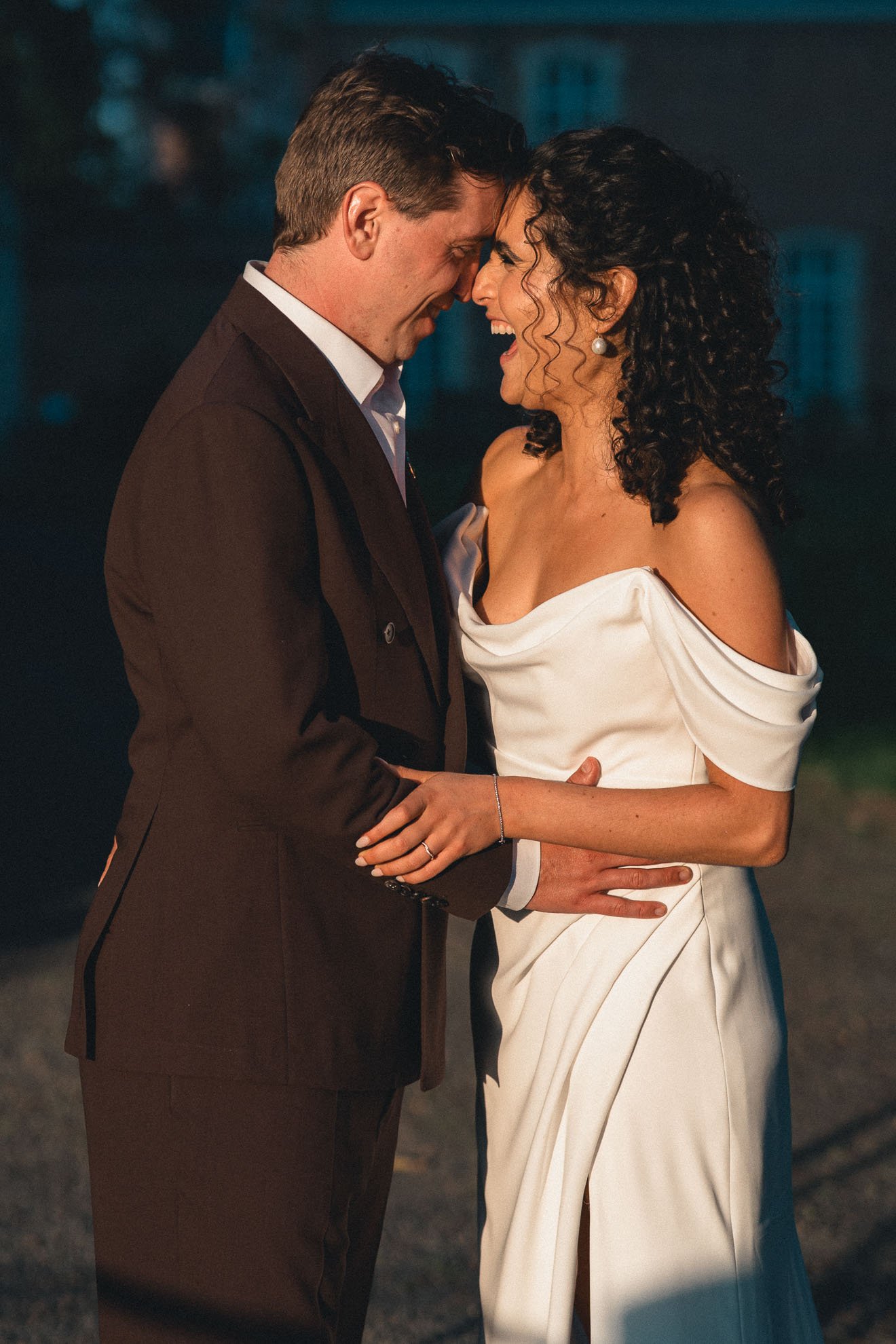 A man and woman are sharing a close, joyful moment with foreheads touching and smiling in an outdoor setting at night.