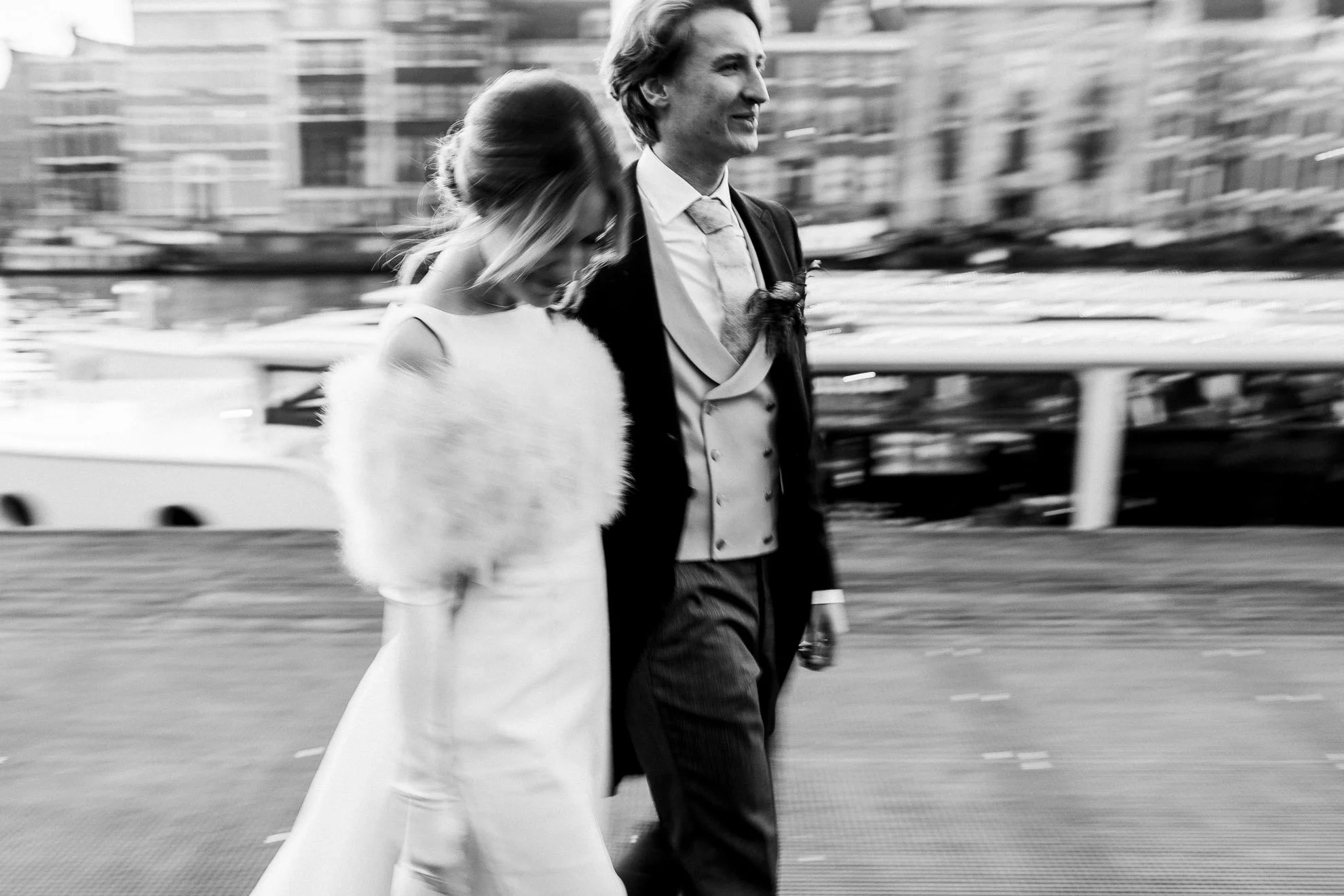 A black-and-white photo of a man and a woman walking together on a city street, with the man wearing a suit and the woman wearing a fur coat.