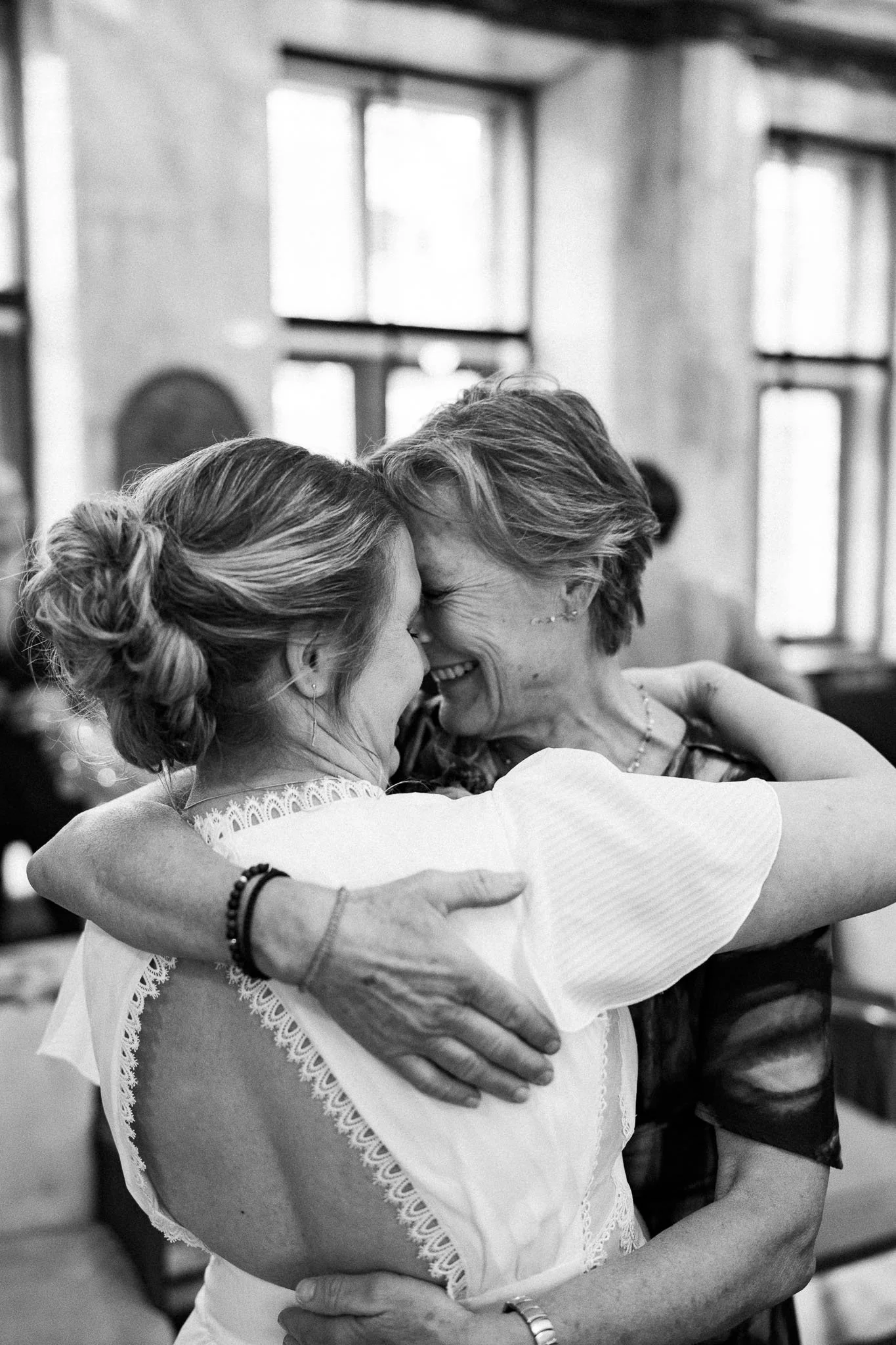 Twee vrouwen omhelzen elkaar liefdevol, gezicht tegen gezicht, lachend, binnen, zwart-wit foto.