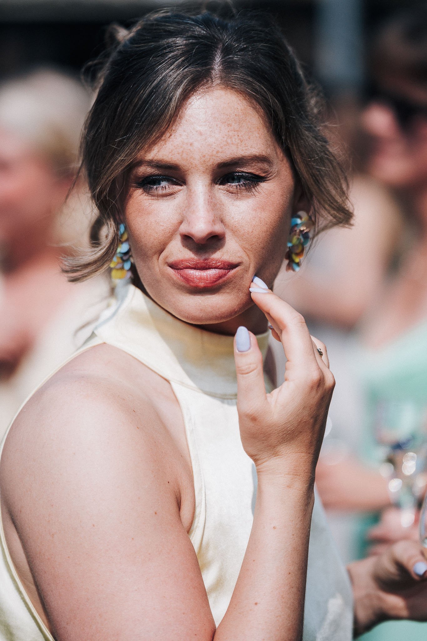 Portret van een vrouw met korte, effen haar, opvallende blauwe oogmake-up en kleurrijke oorbellen, die lijkt te twijfelen of nadenkt.