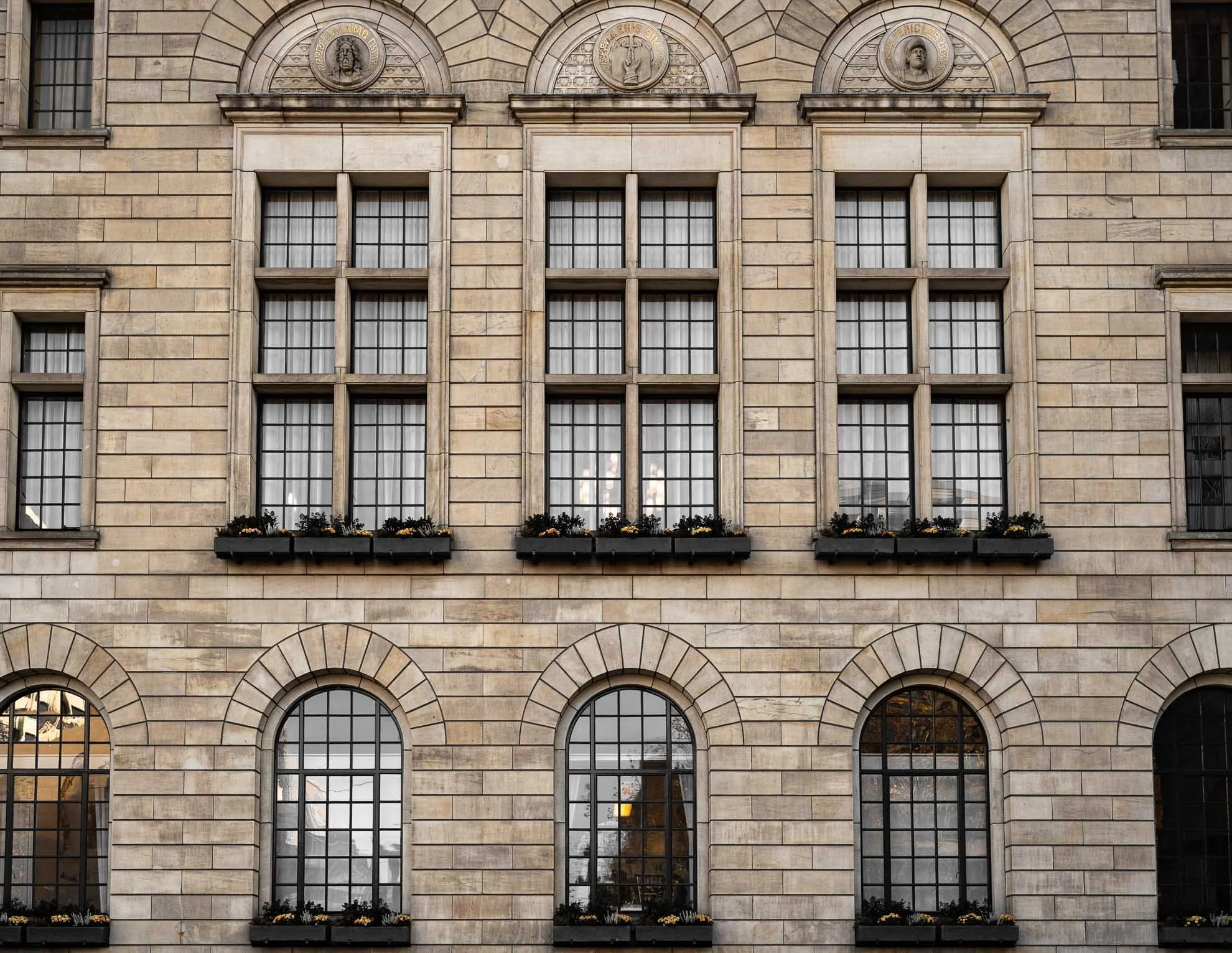 Close-up view of a historic beige stone building with rectangular and arched windows and decorative medallions on the upper facade.