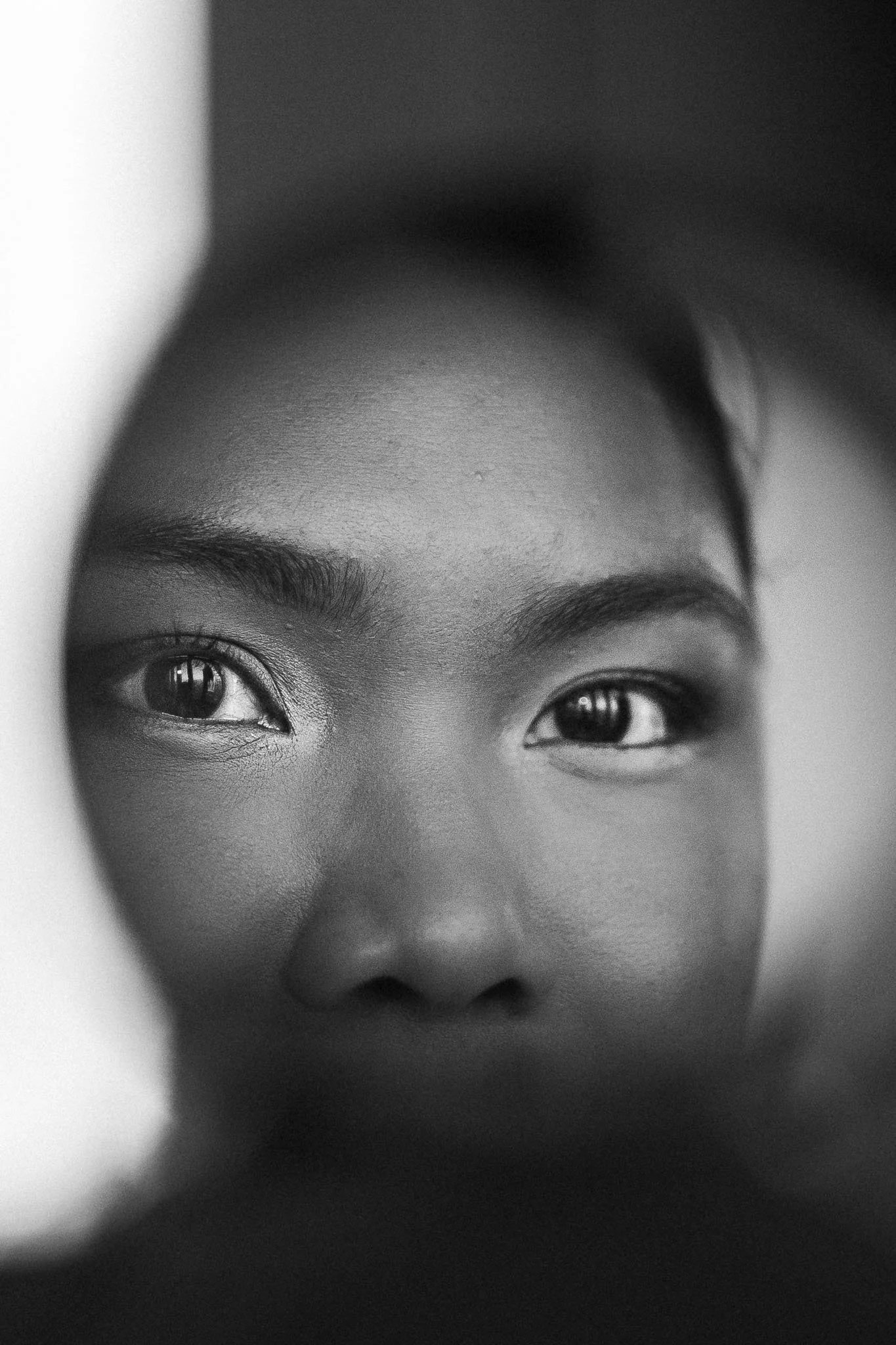 Een close-up zwart-wit foto van een menselijk gezicht, met focus op de ogen die door een ronde opening worden bekeken.