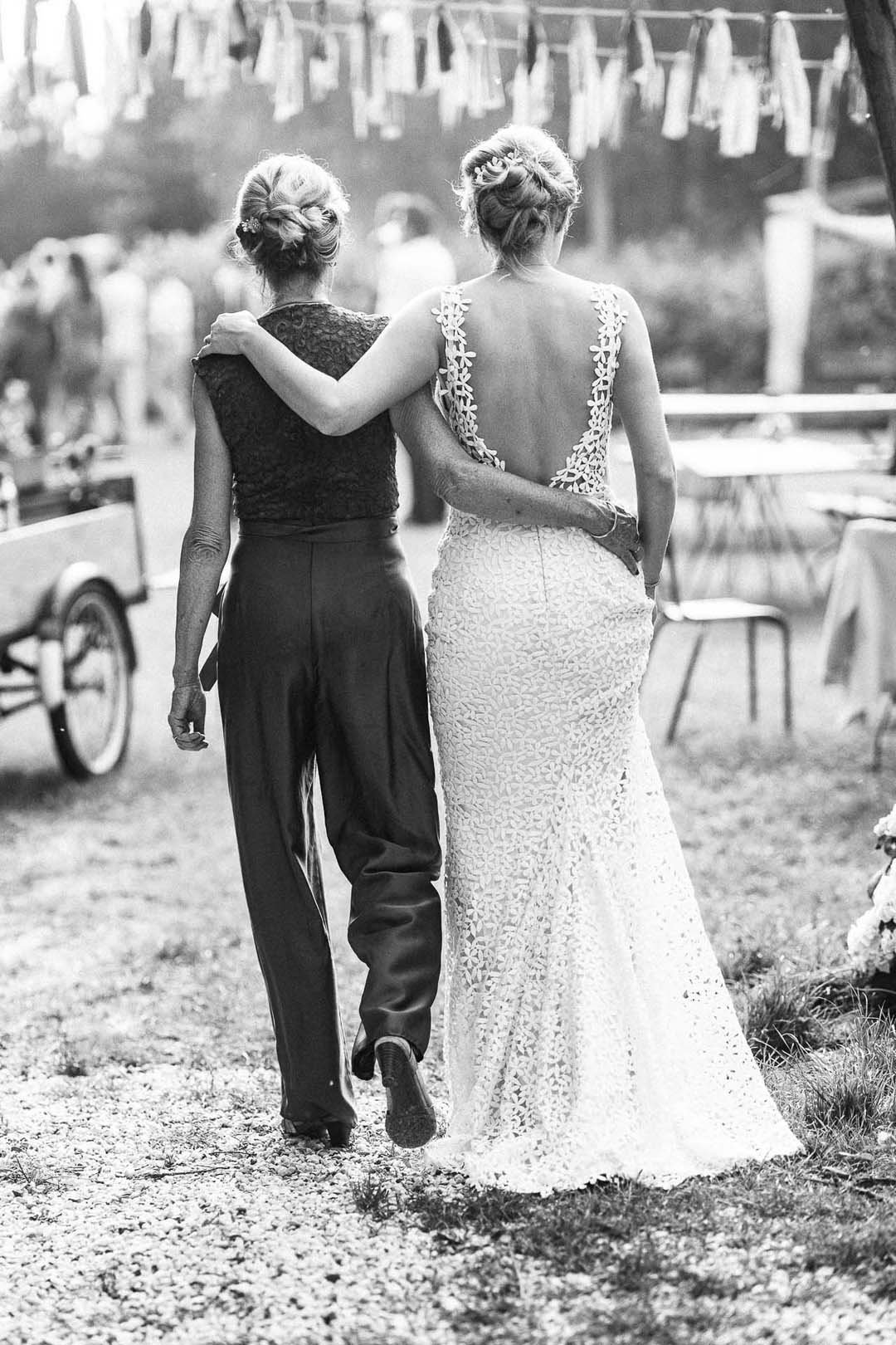 Twee vrouwen lopen hand in hand, een lijkt de bruidsjurk te dragen, tijdens een bruiloft buiten.