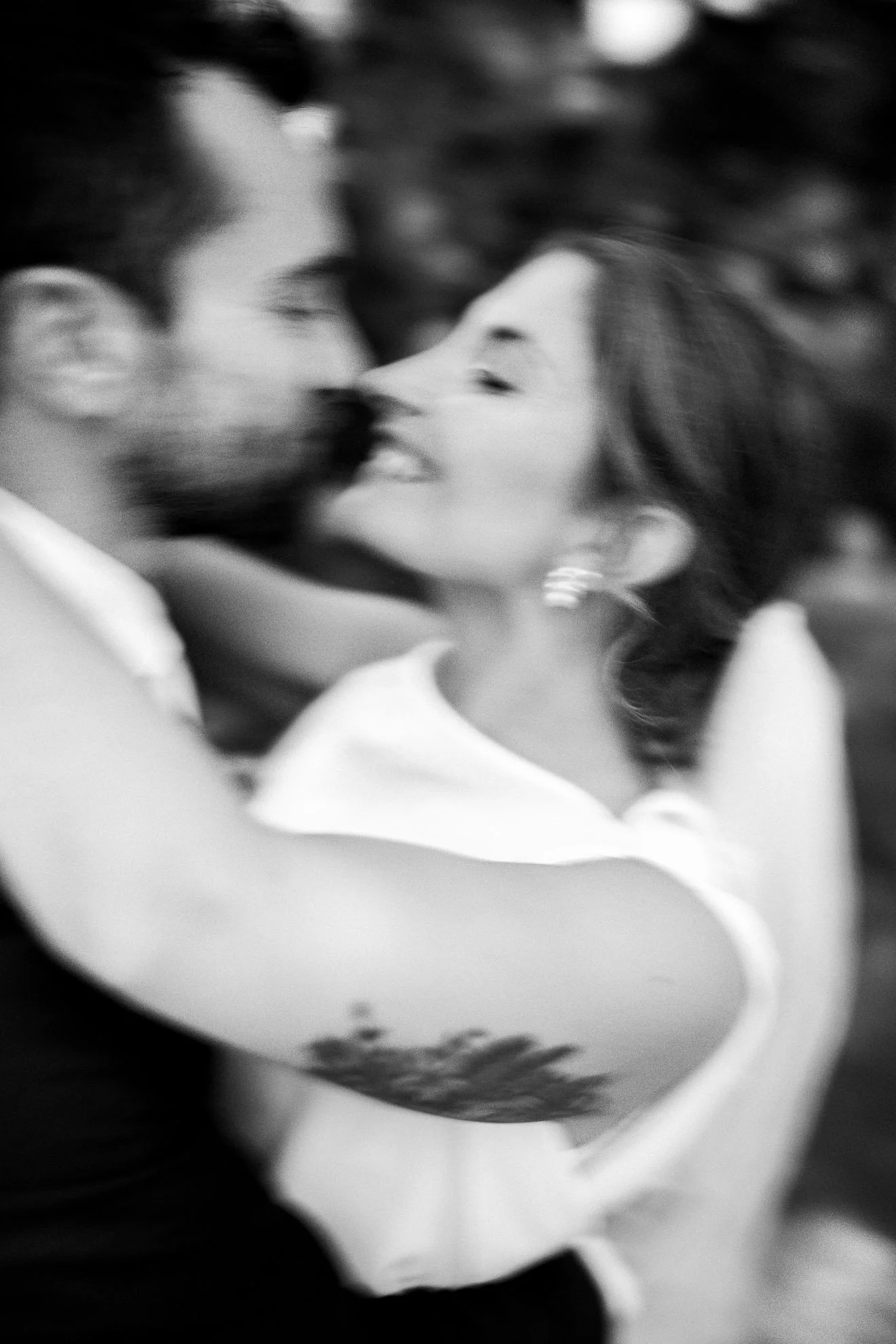 A black and white photo of a couple leaning in close to kiss, with blurred background and soft focus.