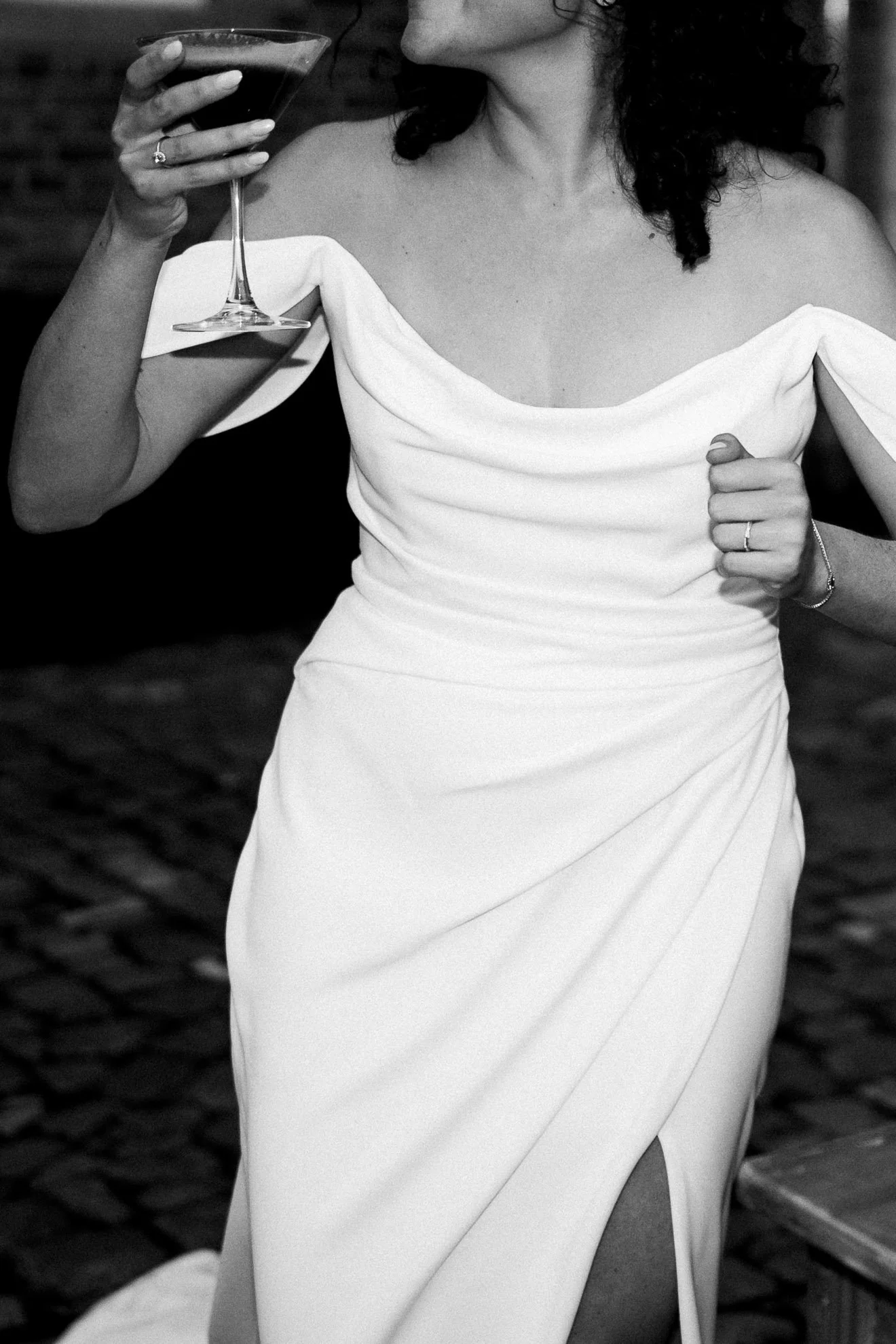 A woman in an off-shoulder white dress holding a martini glass in her right hand.