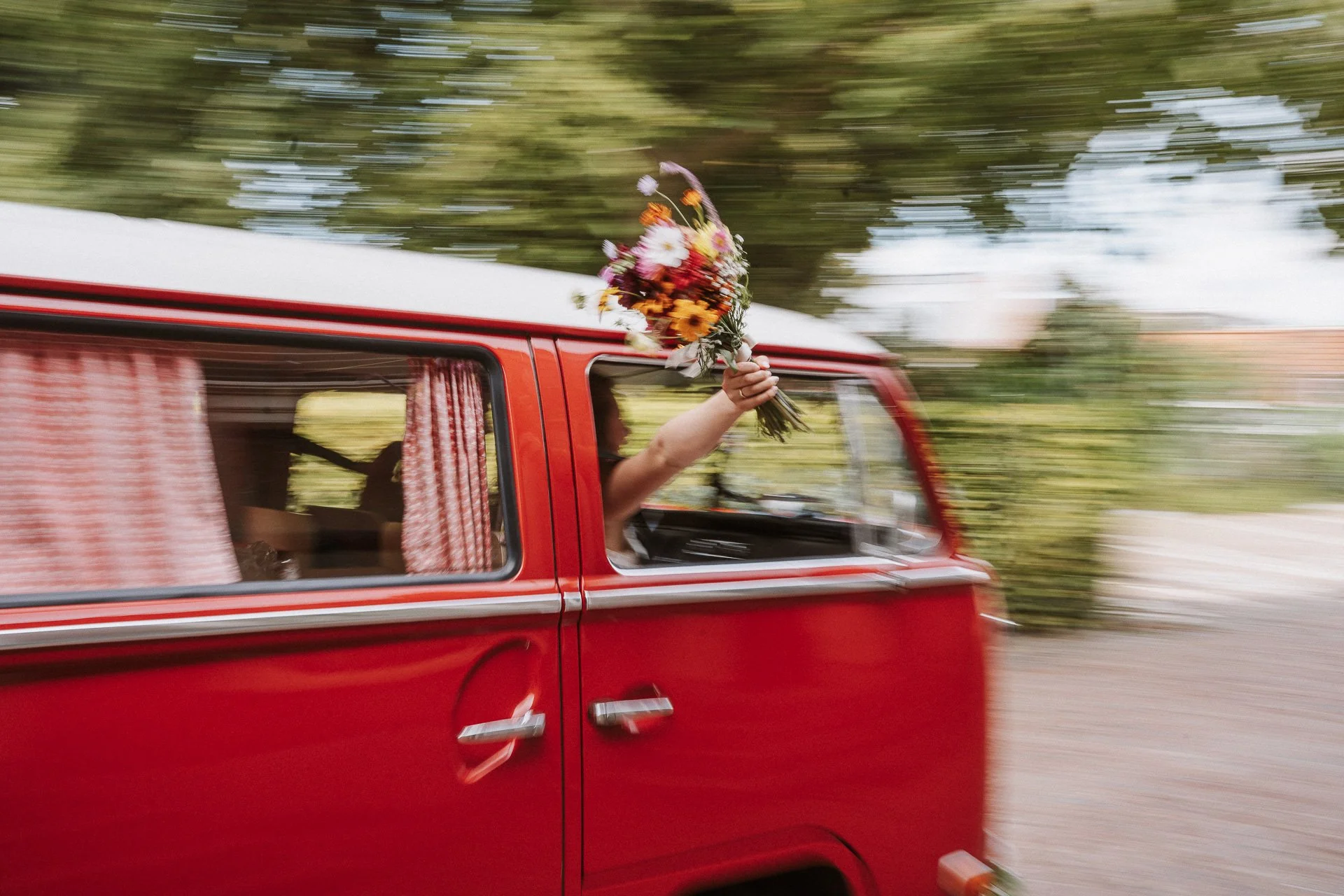 Persoon steekt arm uit een rood busje en houdt een bloemenboeket omhoog.