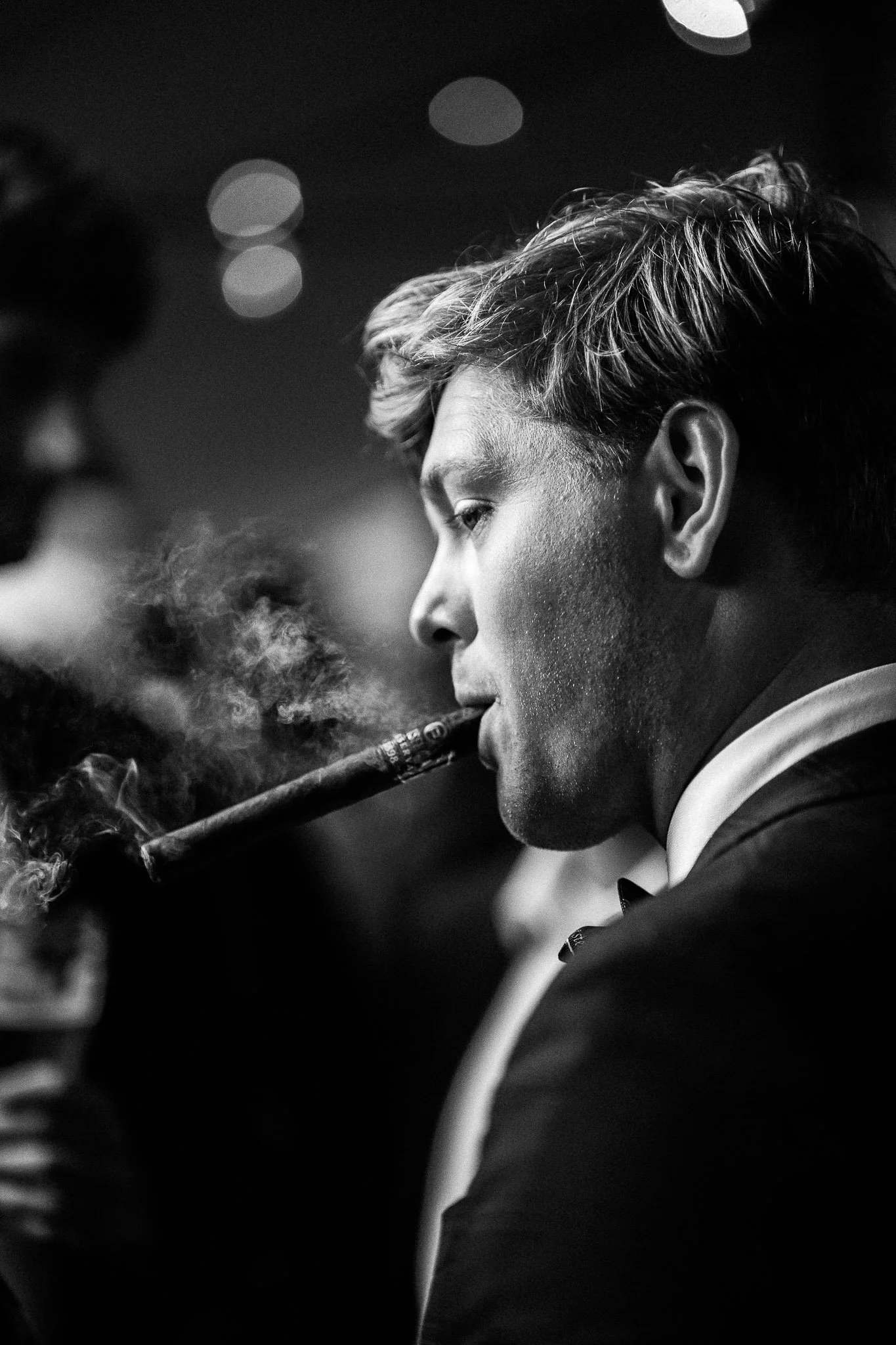 Zwart-wit foto van een jonge man in een pak die een sigaar rookt.