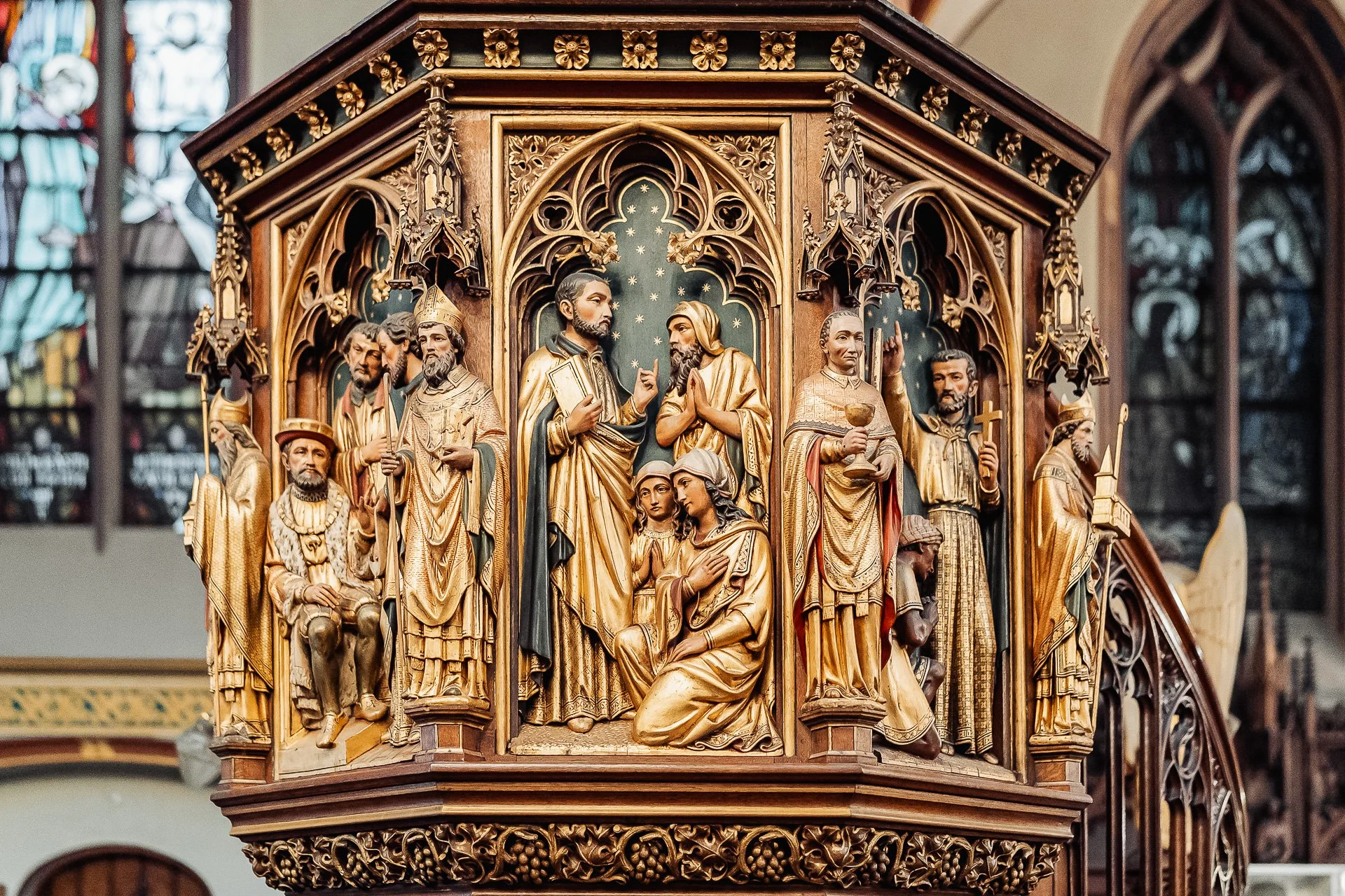 Kunstwerk in een kerk, met meerdere heiligen en bijbelse figuren in gouden en gekleurde details.