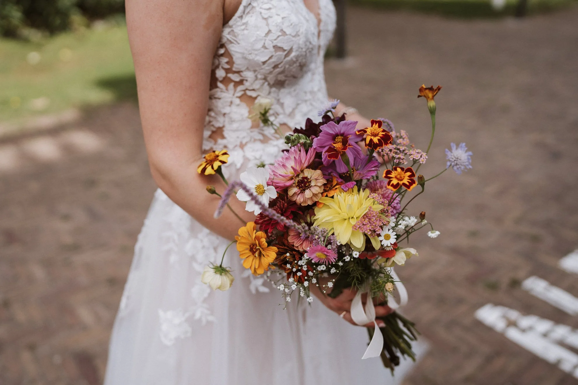 A bride in a white lace wedding dress holding a colorful bouquet of flowers