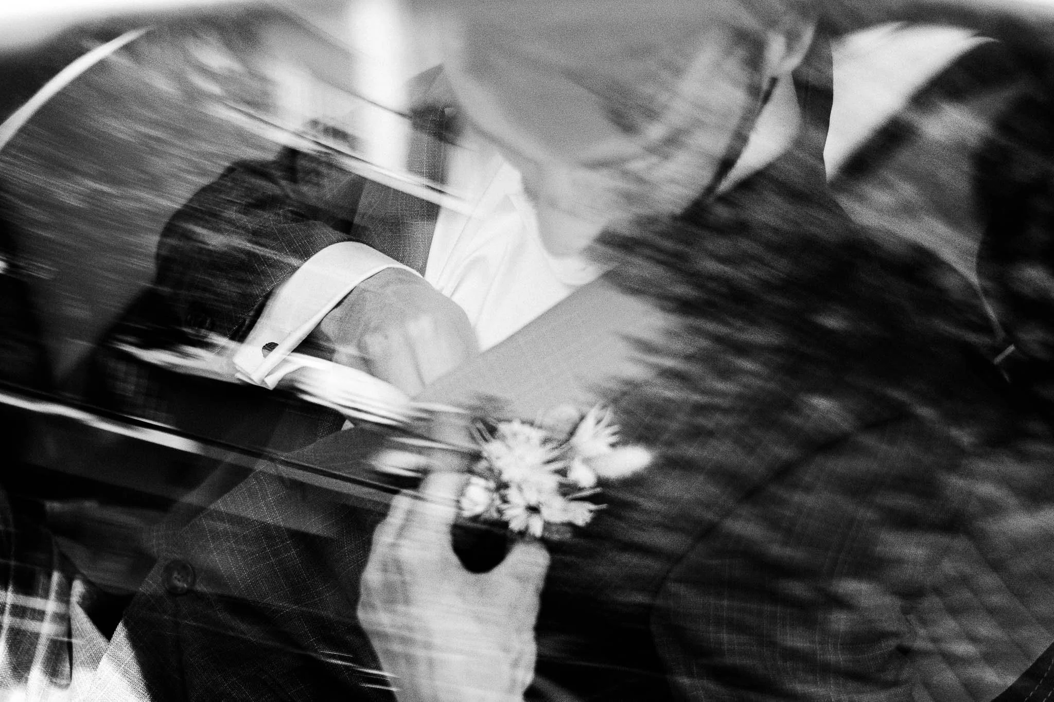 Een zwarte en witte foto van een persoon die met een pen schrijft op een notitieboekje, met een blazer en een bloem op de jas.