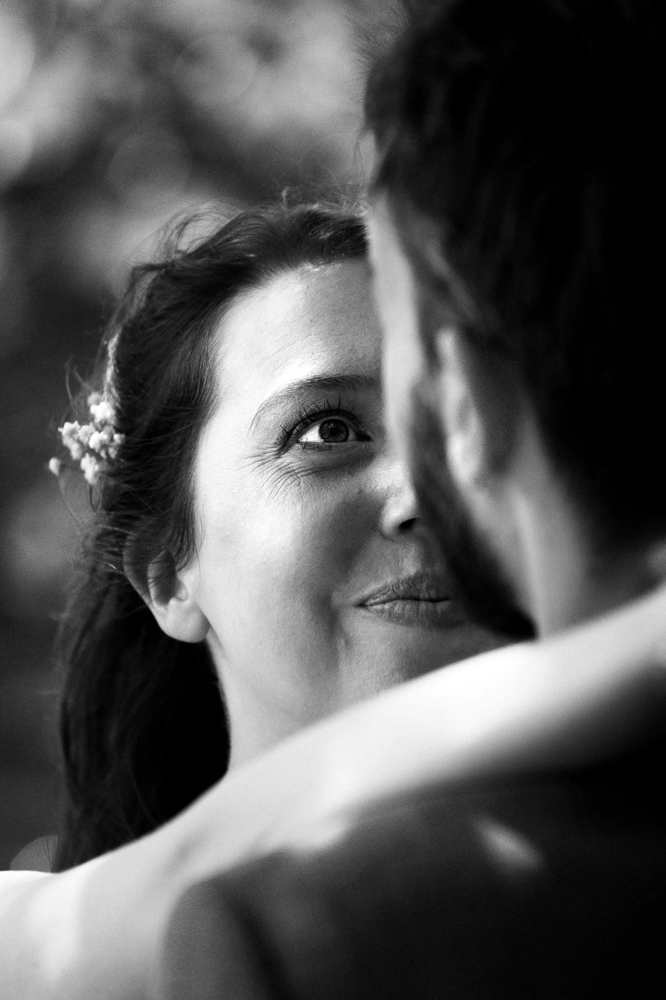 Zwart-wit foto van een vrouw die lacht en haar partner omhelst, haar rechteroog en glimlach duidelijk zichtbaar.