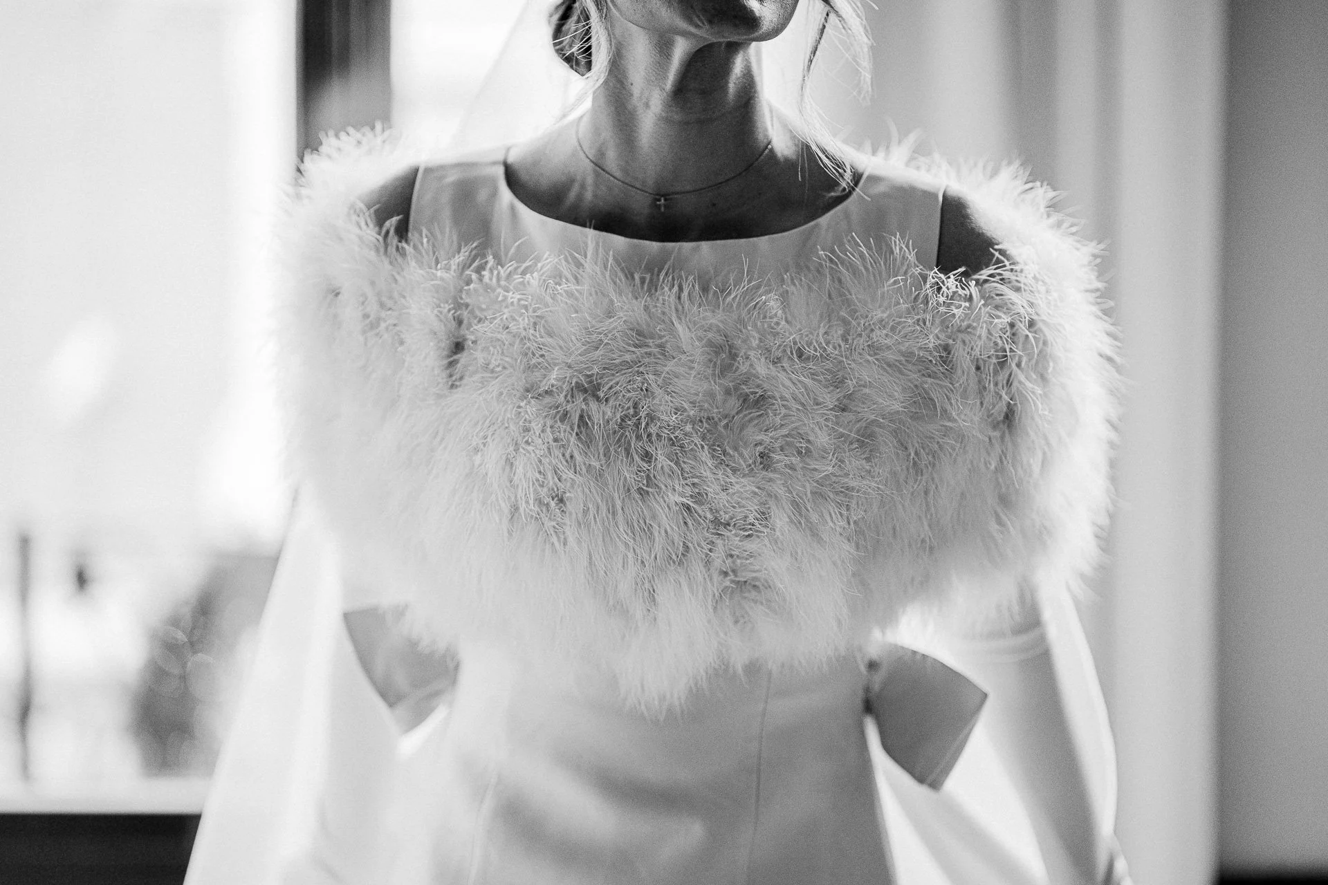 Een zwart-wit foto van een vrouw die een witte jurk draagt met een grote, pluizige, zijden en verenachtige schouderaccessoire.