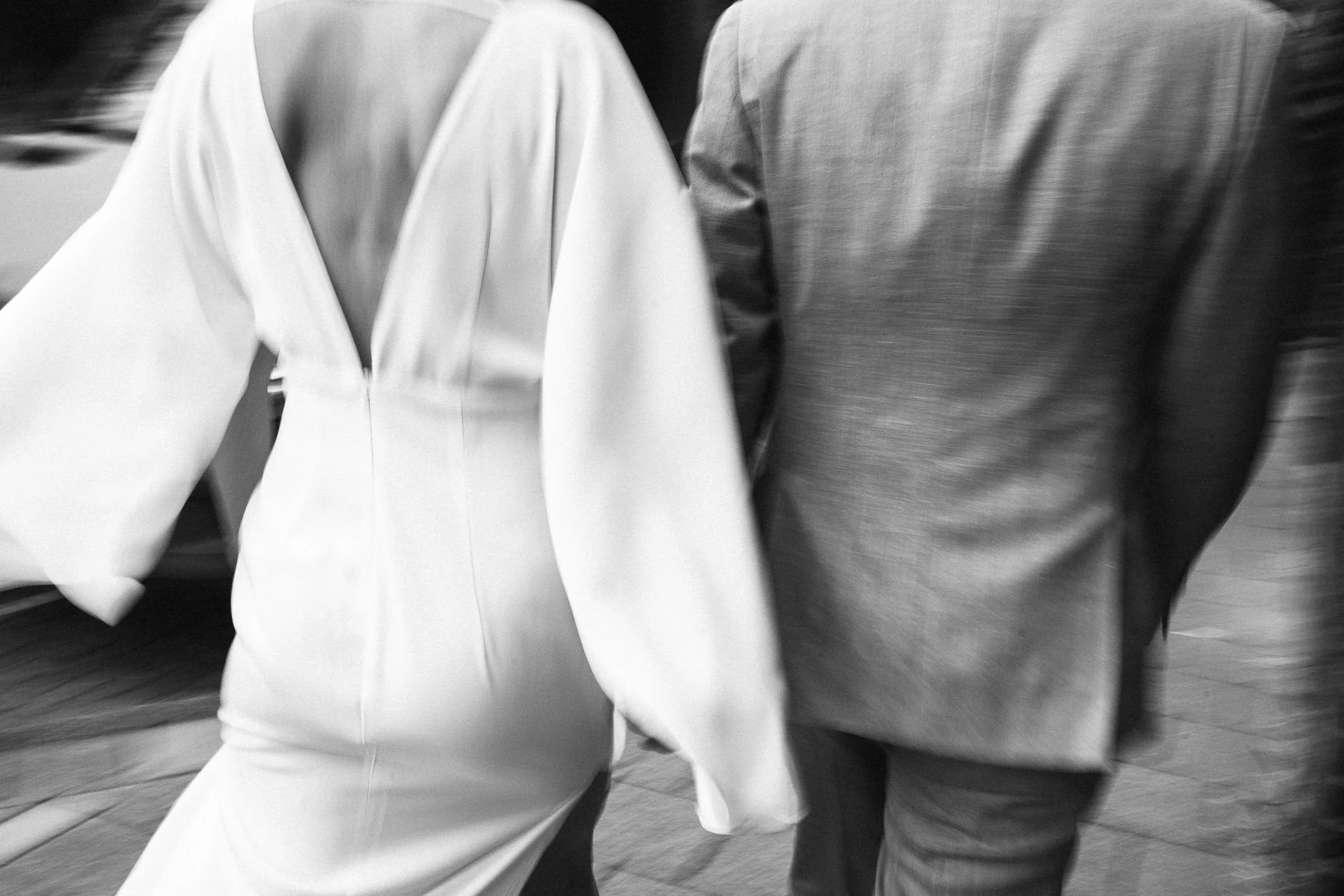Close-up of two people walking side by side, wearing long-sleeved tops. One in a light-colored top and the other in a darker top. The photo is in black and white, capturing motion.