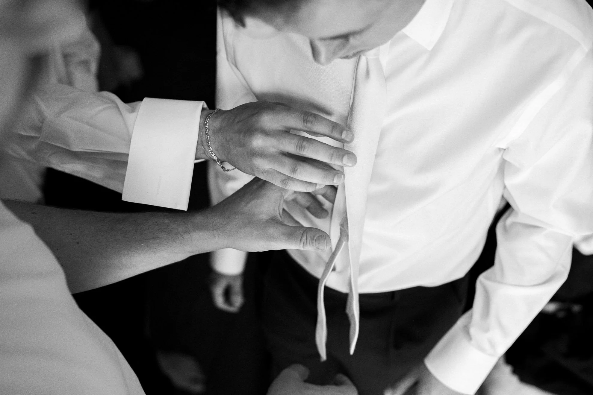 Black and white image of a person in a white shirt being helped by another person wearing a bracelet as they perform CPR or first aid on the person's chest.