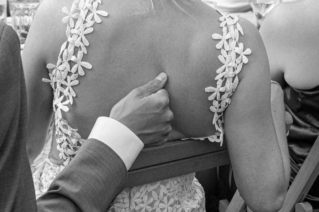 Een hand die op een vrouw haar borst ligt tijdens een ceremonie, gekleed in een jurk met bloemmotief.