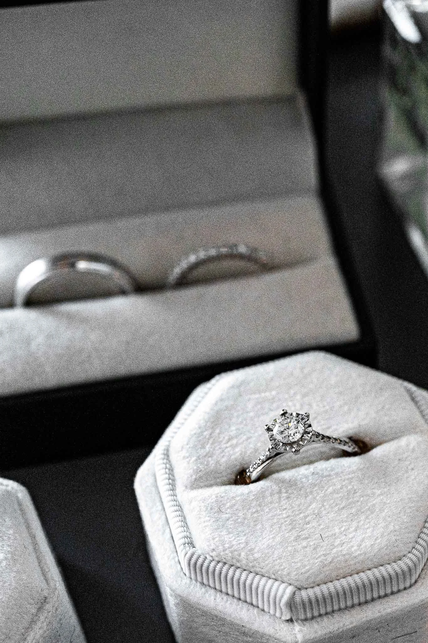 Een verlovingsring met een grote centrale diamant in een gespreide ring met kleine diamanten, geplaatst in een witte ringendoos.