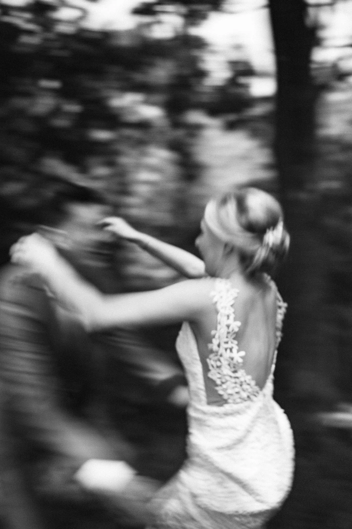 Een vrouw in een witte jurk met bloemdetails, danst of rent in beweging, met een bos of park op de achtergrond, zwart-wit foto.