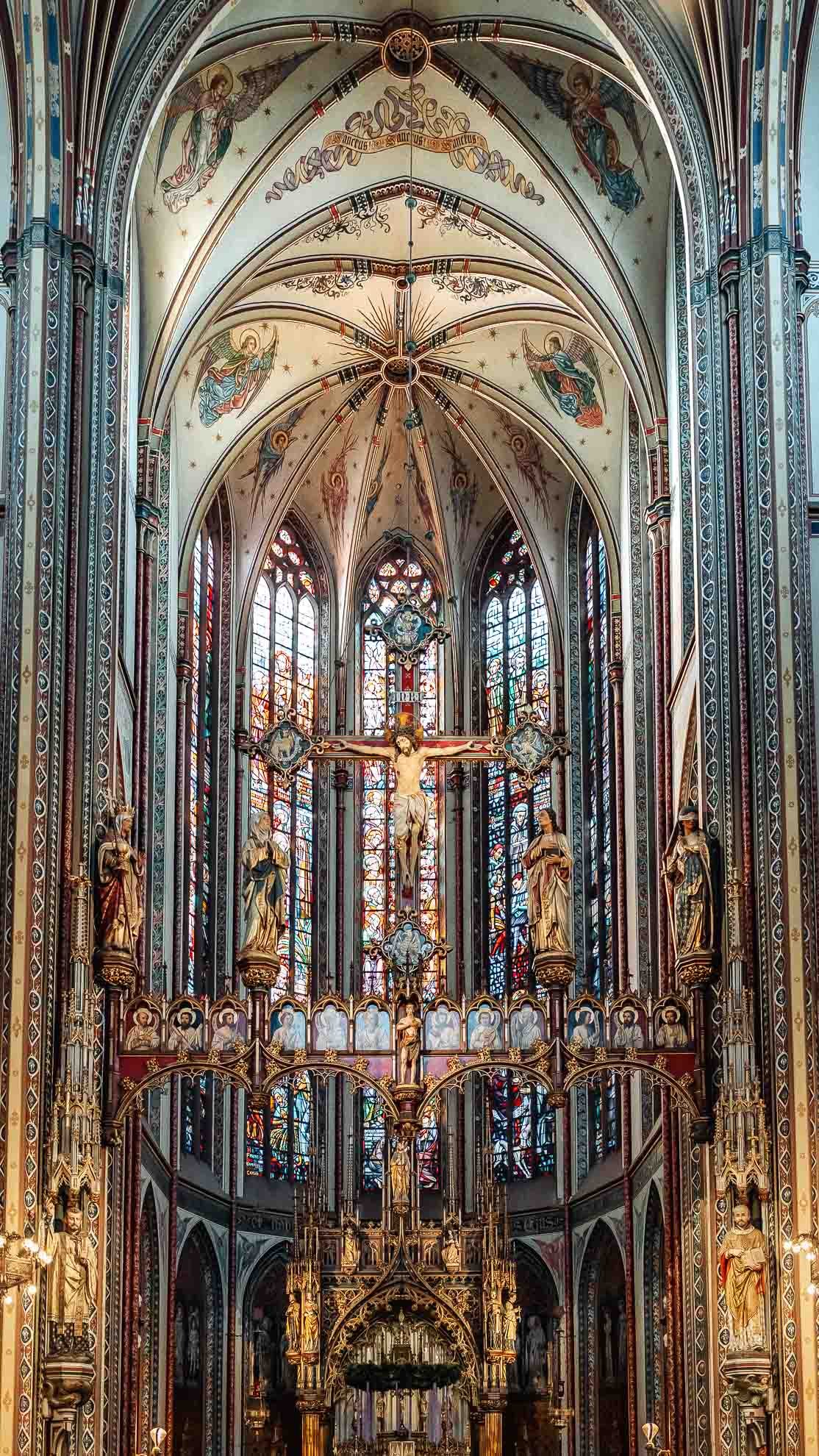 Interior of a gothic-style church with stained glass windows, religious statues, and a crucifix in the center.