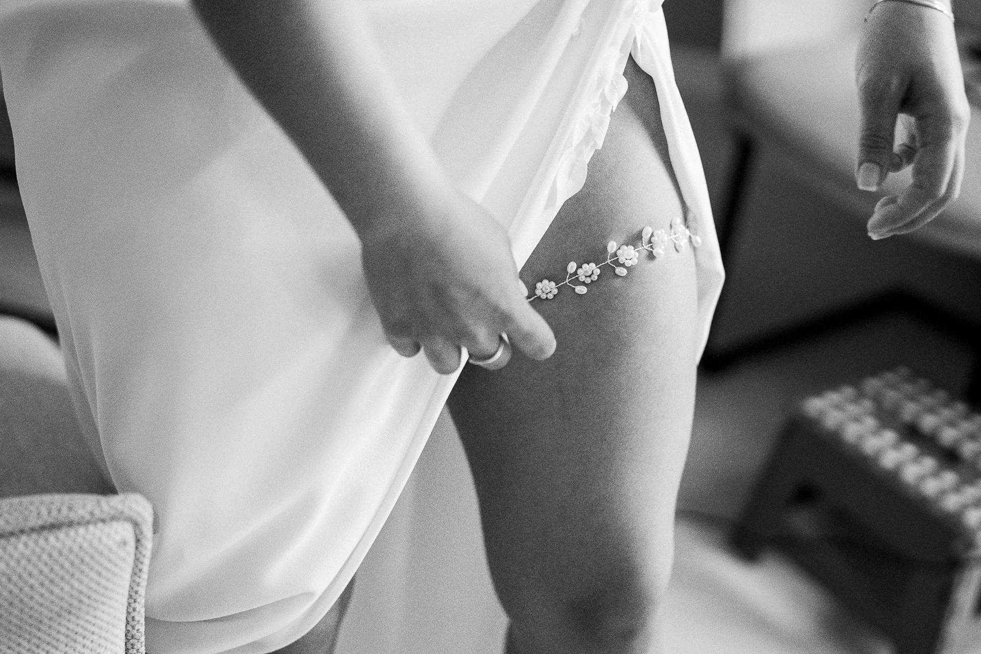 Zwarte en witte close-up van een bruid die haar witte jurk aanpast met een bloemrijke onderbroek