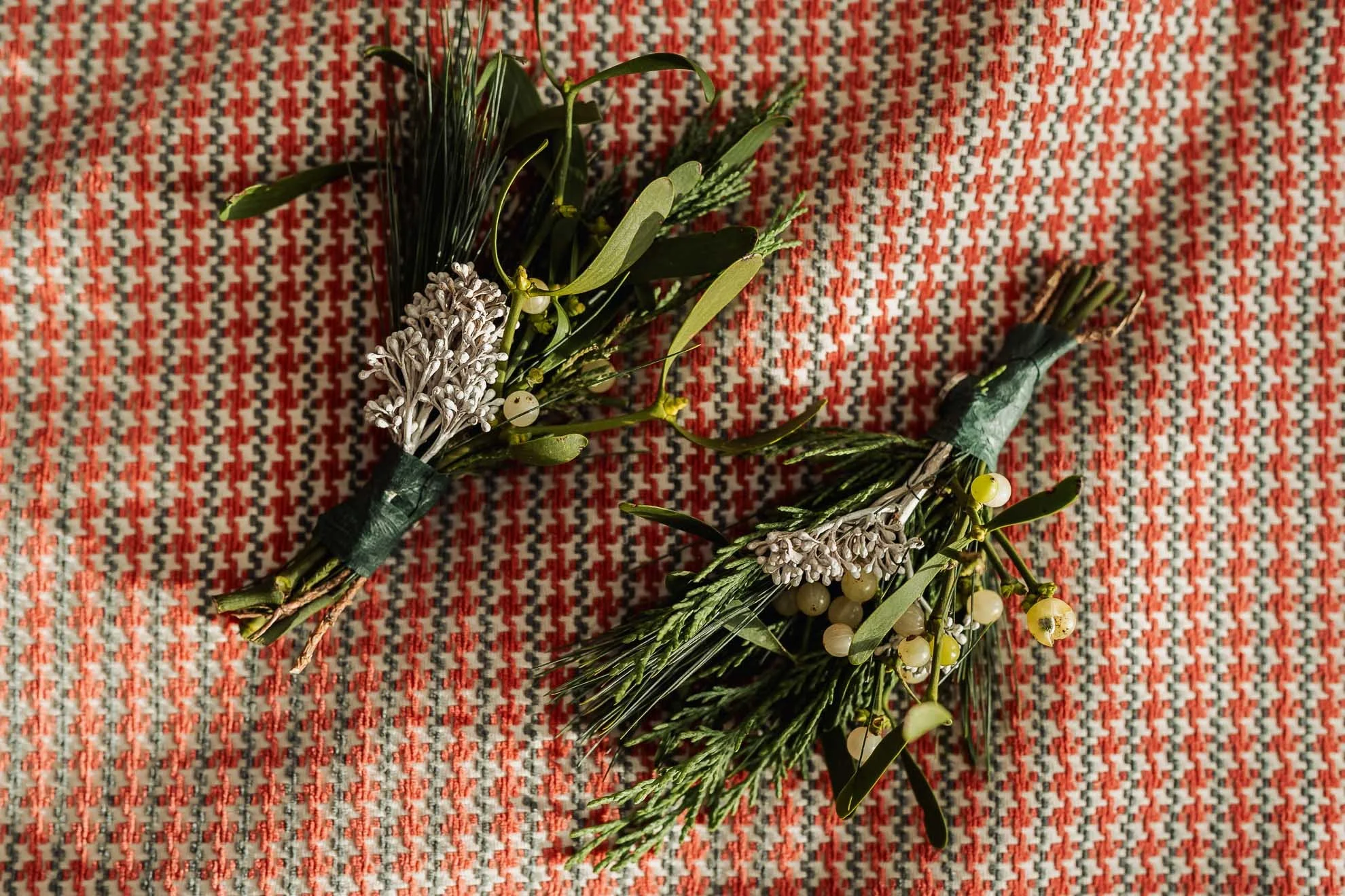 Artificial wreath with greenery, white flowers, and small white berries resting on a red, white, and black patterned fabric.